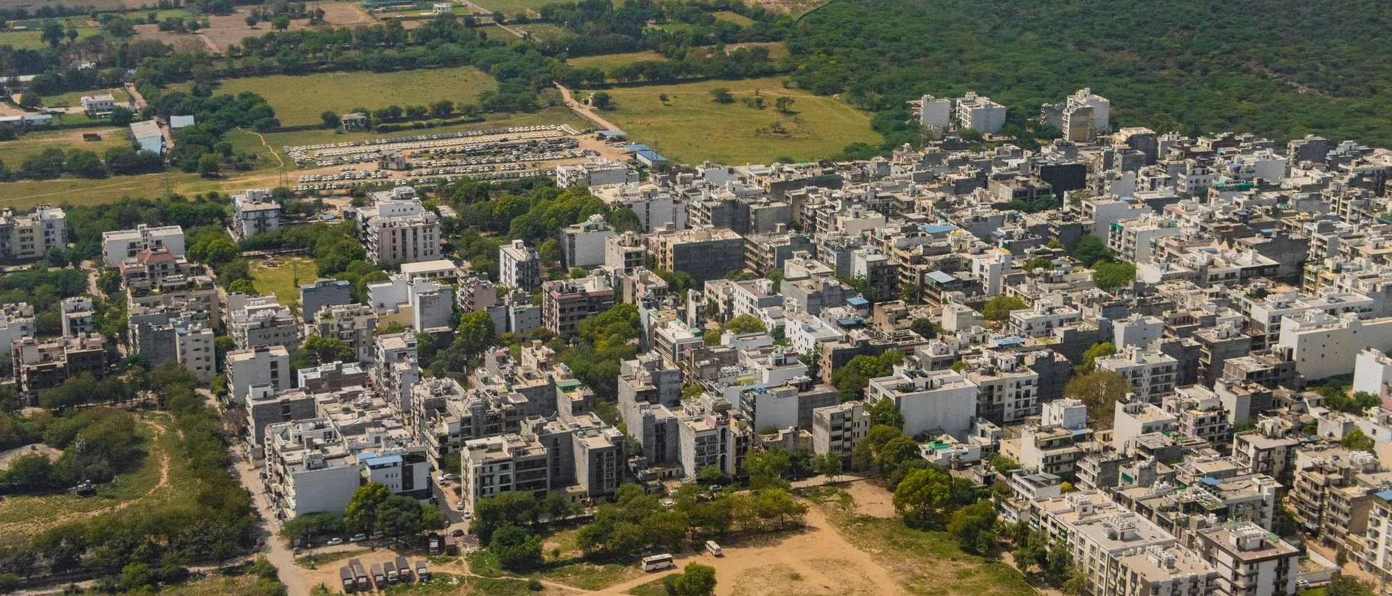 An aerial view of Gurugram’s towers and roads with green land beyond.