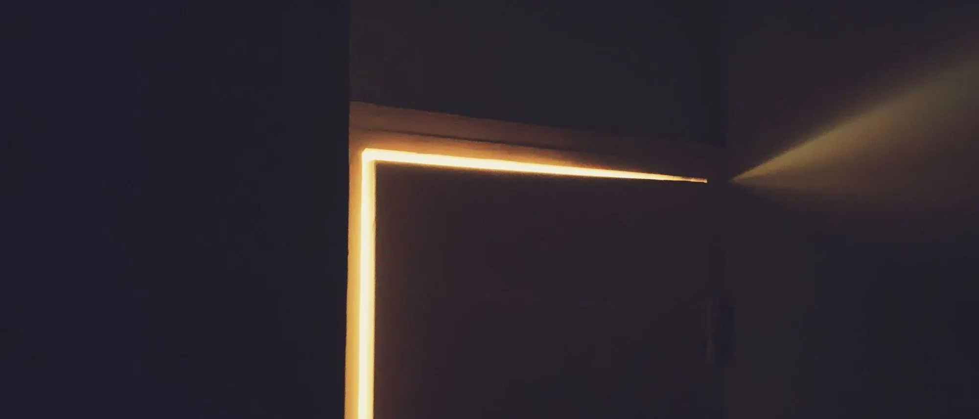 Warm light spills through a door left slightly open into a dark room.