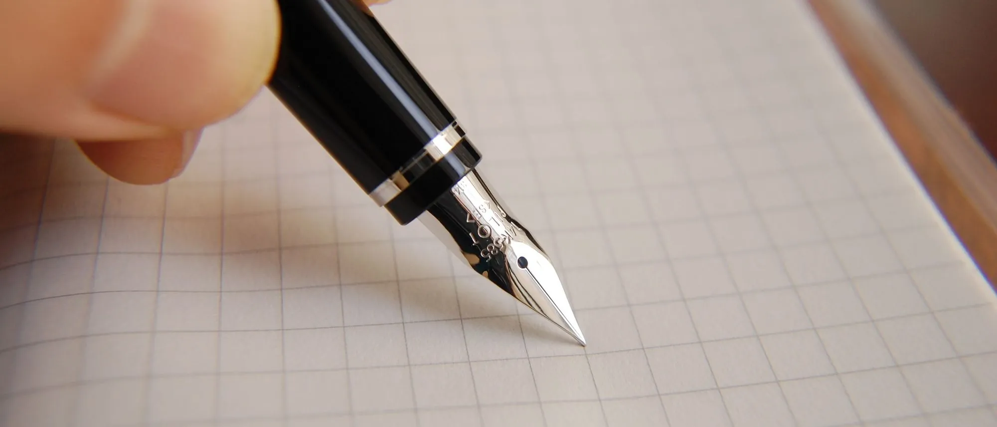 A fountain pen poised over a sheet of graph paper.