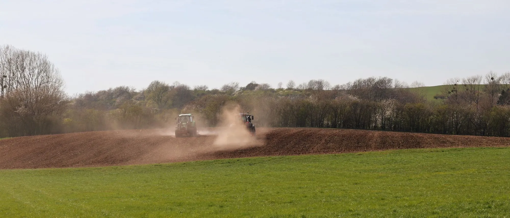 A tractor ploughing a wide field under a clear blue sky.