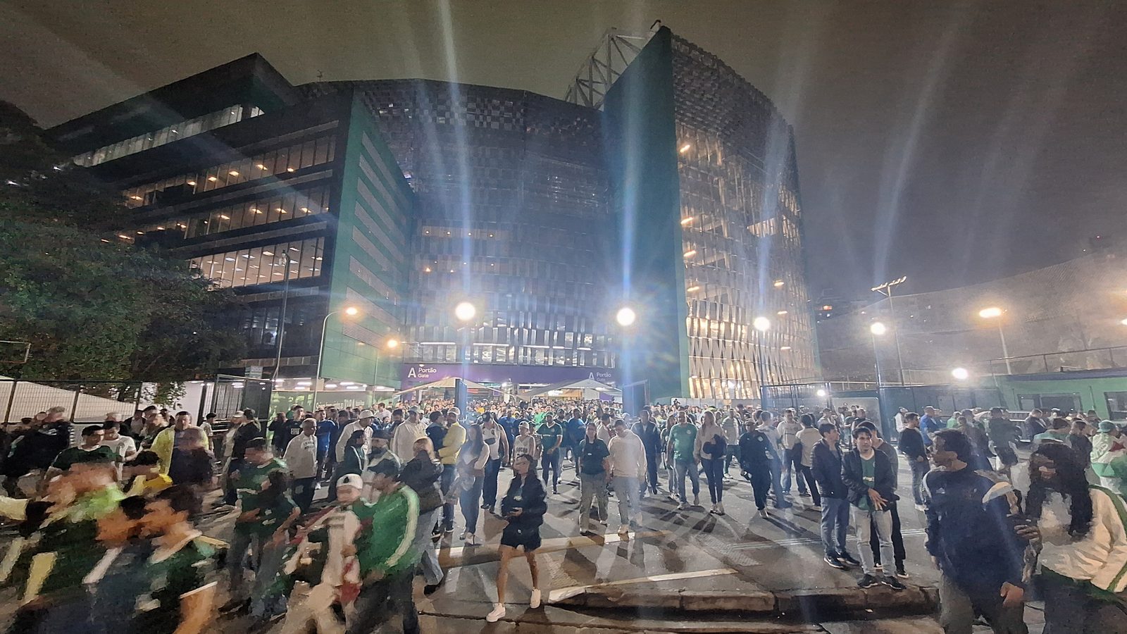 The glass facade of the Nubank Parque stadium in São Paulo lit at night with crowds outside