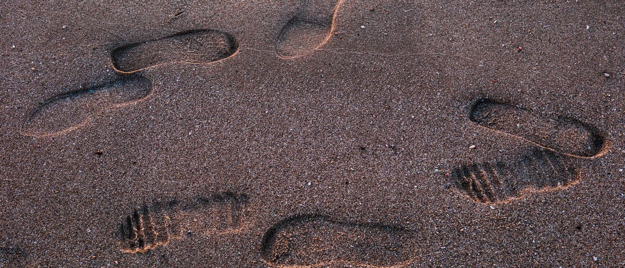 Footprints cross beach sand in the low light of sunset.