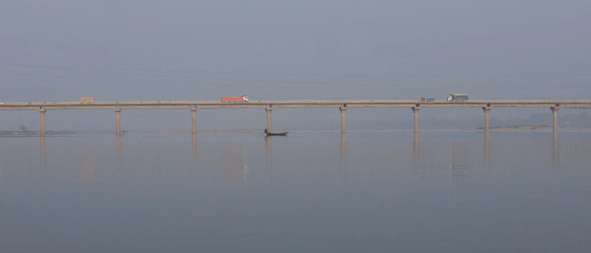 A long bridge crosses a calm river in fog near Chandrapur, its piers reflected in the water.