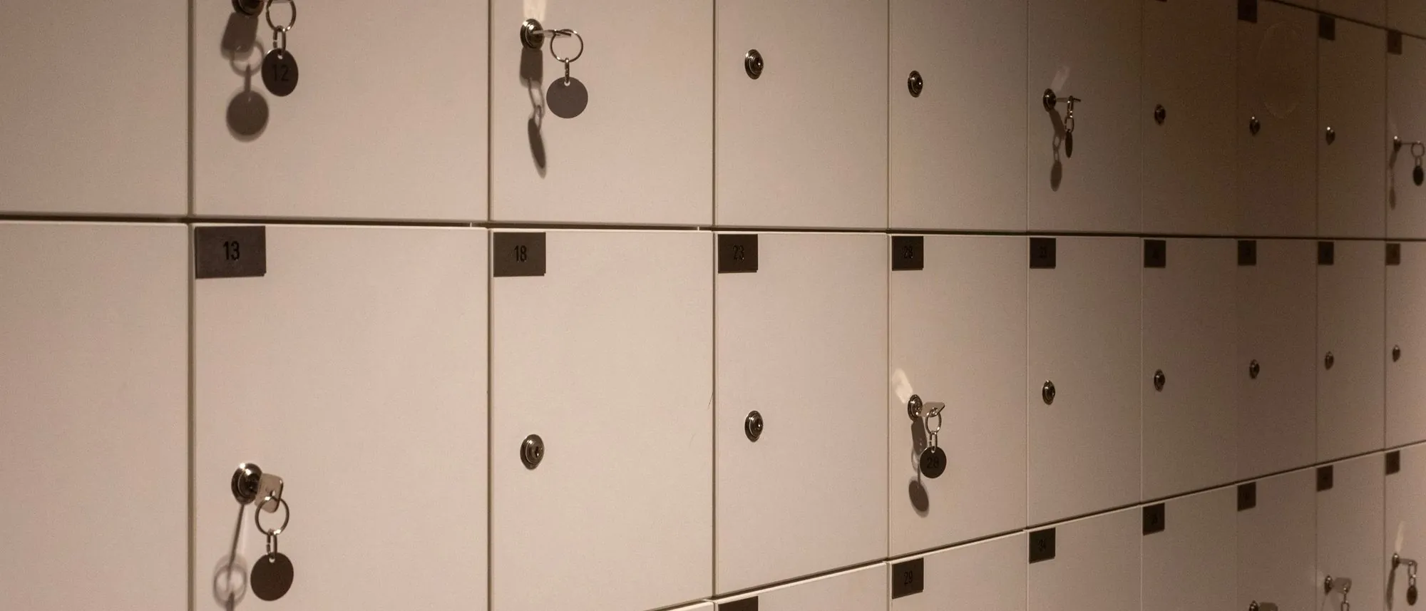 Rows of metal lockers with keys in their doors form a grid in a dim corridor.