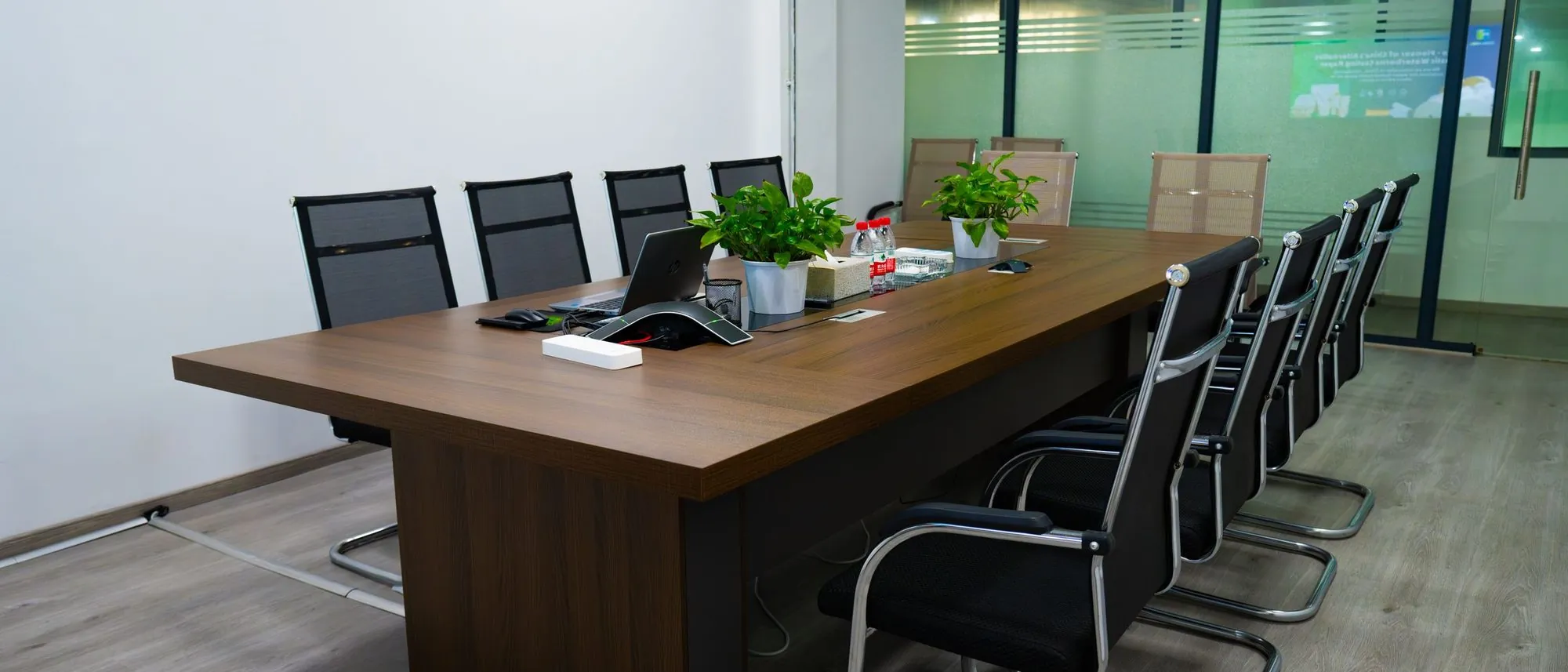A long table with modern chairs and potted plants in an empty conference room.