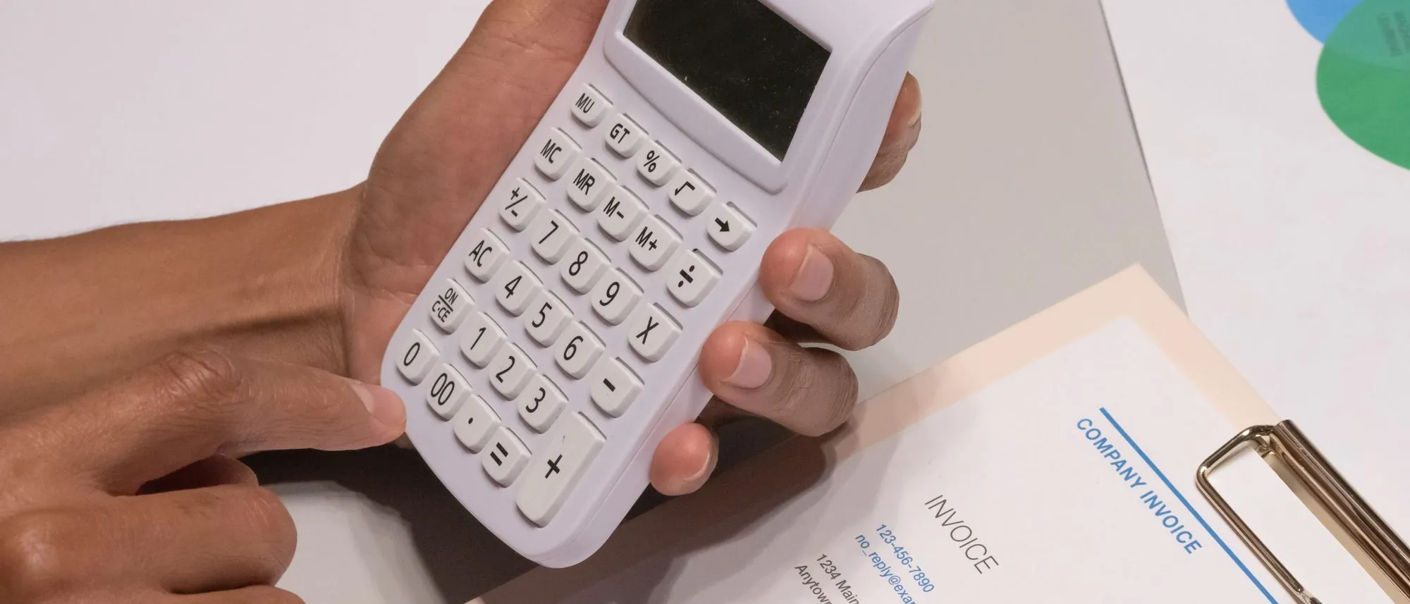 A hand working a desk calculator beside a printed invoice
