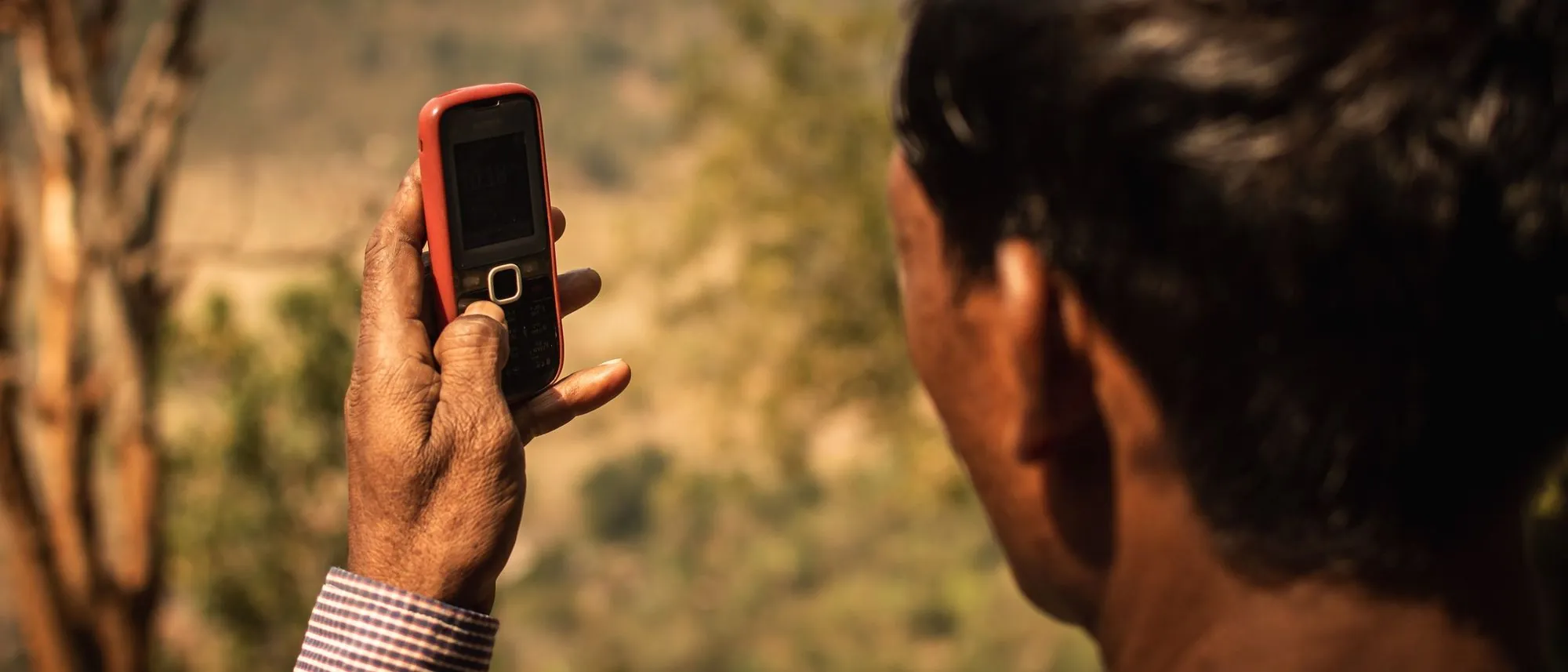 A man holds a mobile phone outdoors in rural Odisha.