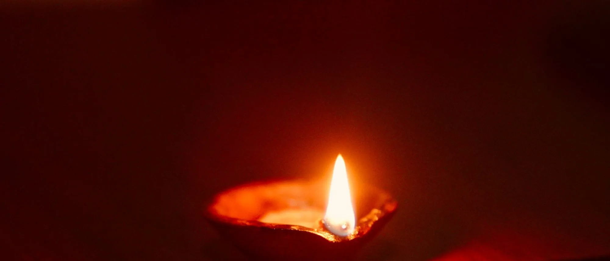 A single oil lamp burning on a wooden surface in the dark.