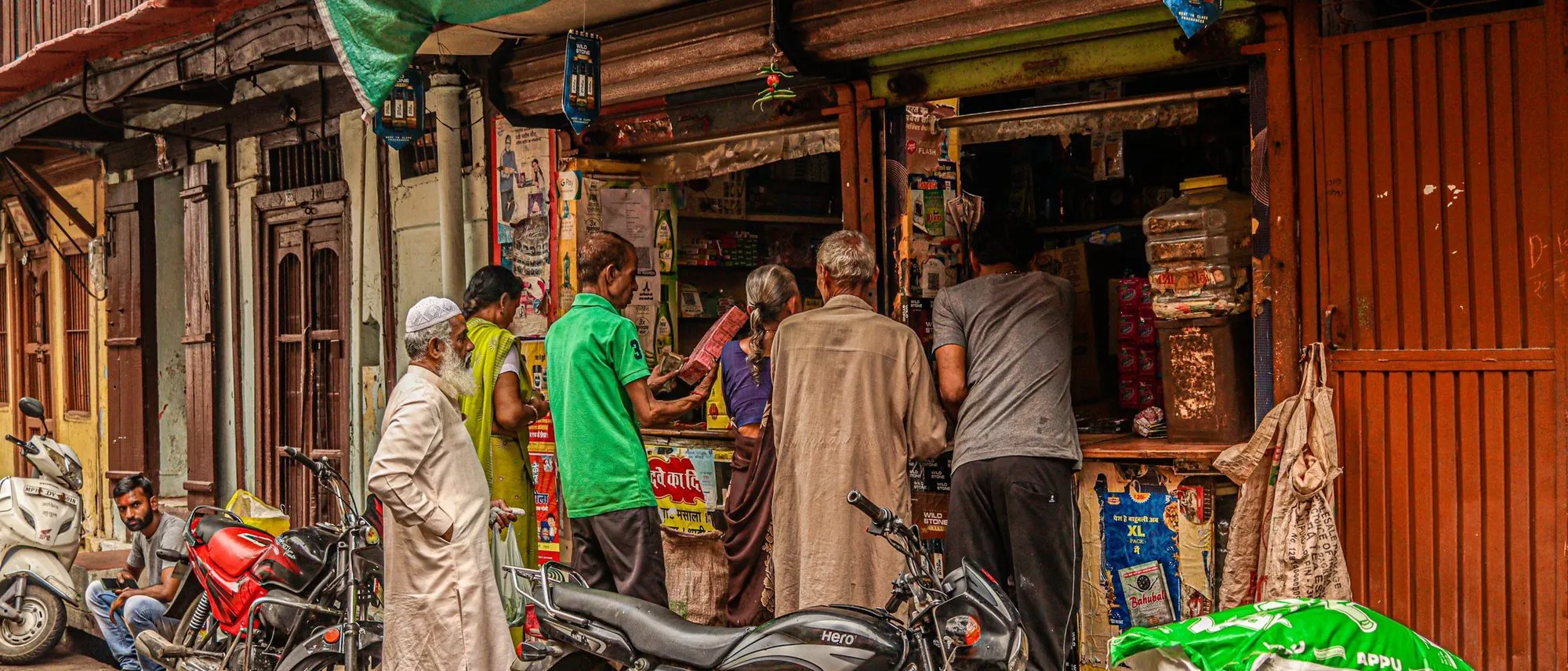A busy street shop in India with customers at the counter and motorcycles parked outside.