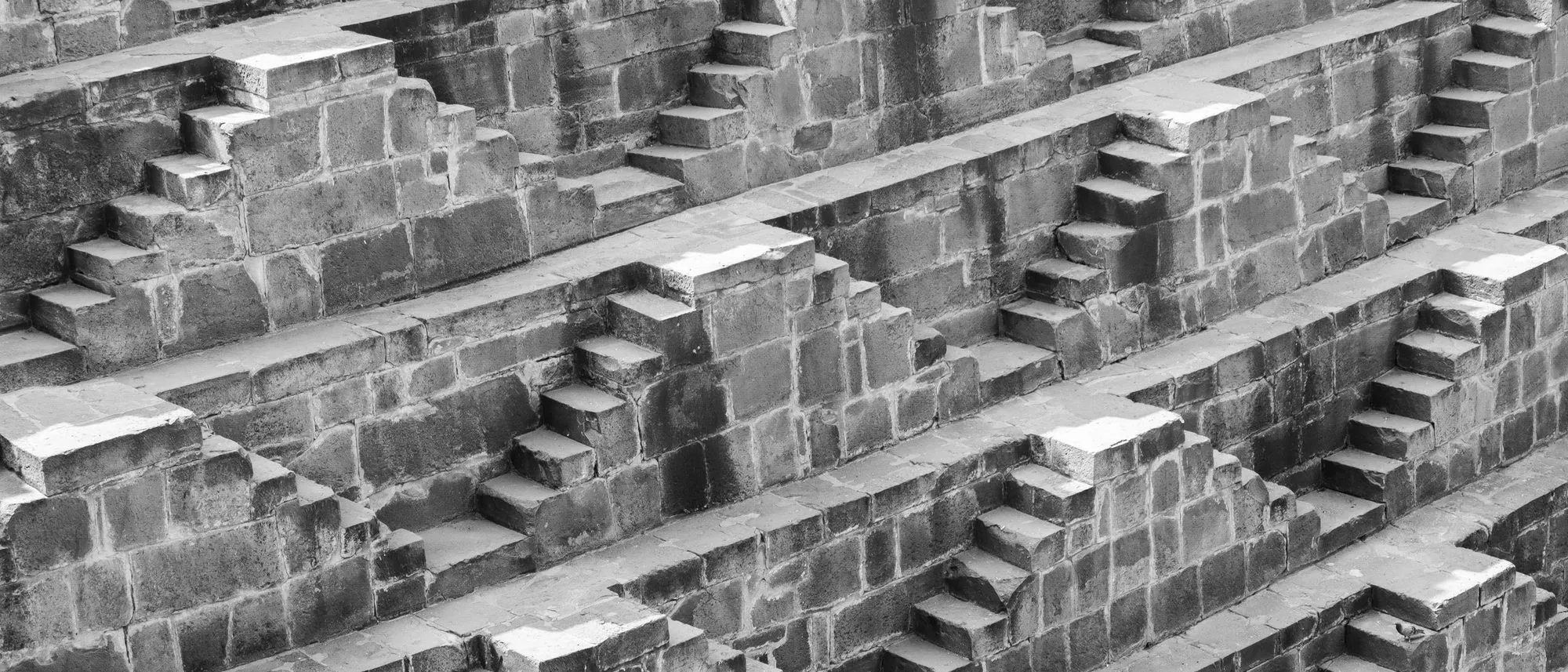 Stone stairways descend in layers down the walls of a stepwell in Bandikui in black and white.