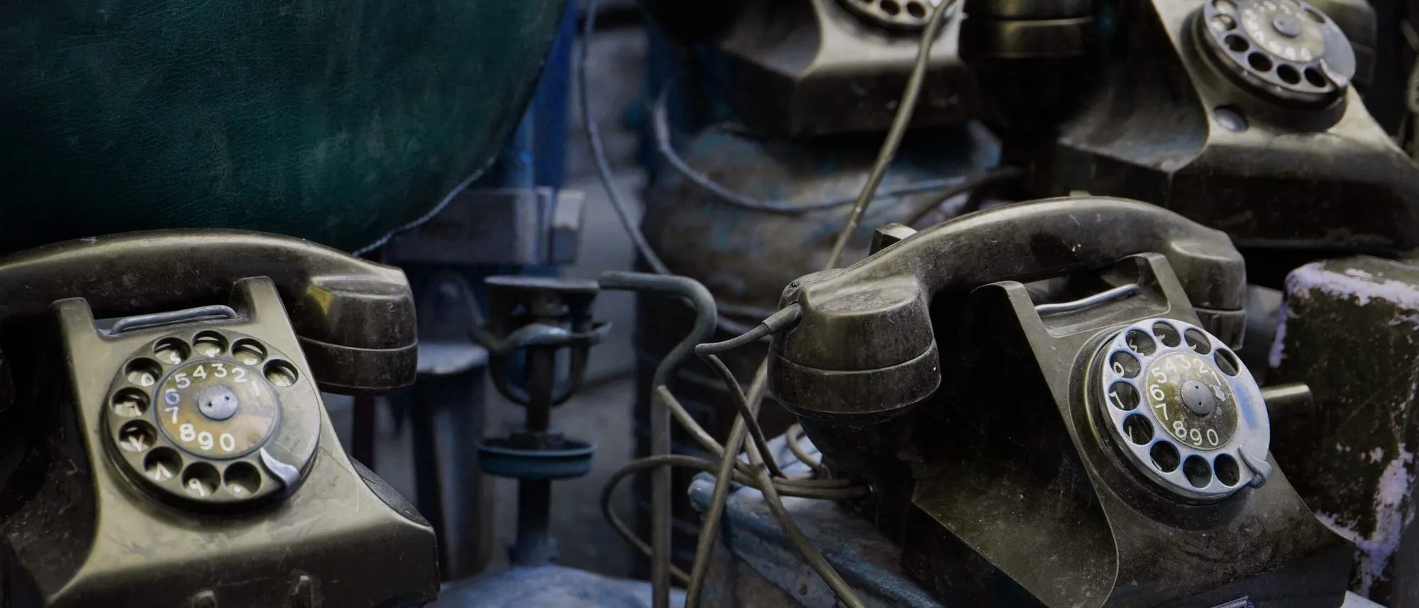 Vintage rotary telephones sit side by side in close-up indoors.
