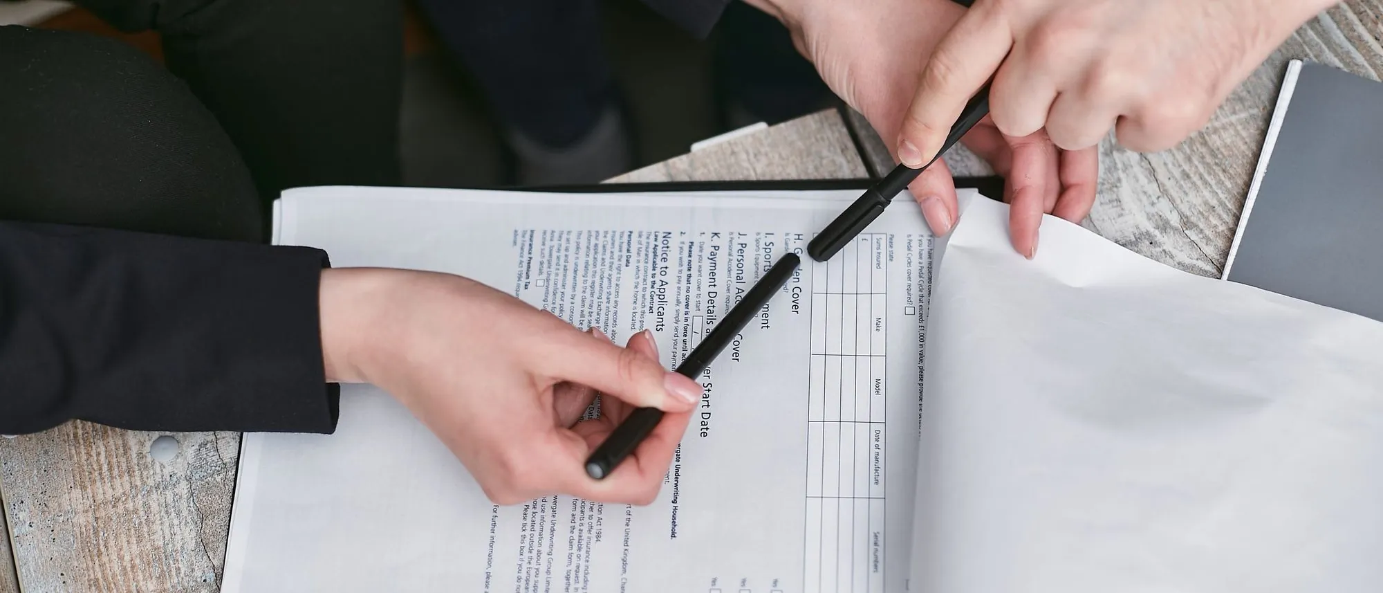 Hands holding a black pen over a printed agreement on a desk.