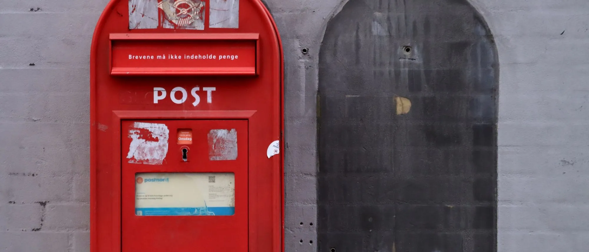 A red post box mounted on a grey urban wall.