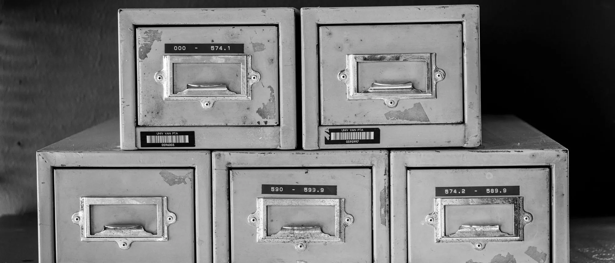Five worn metal filing cabinets stand in a row in black and white.