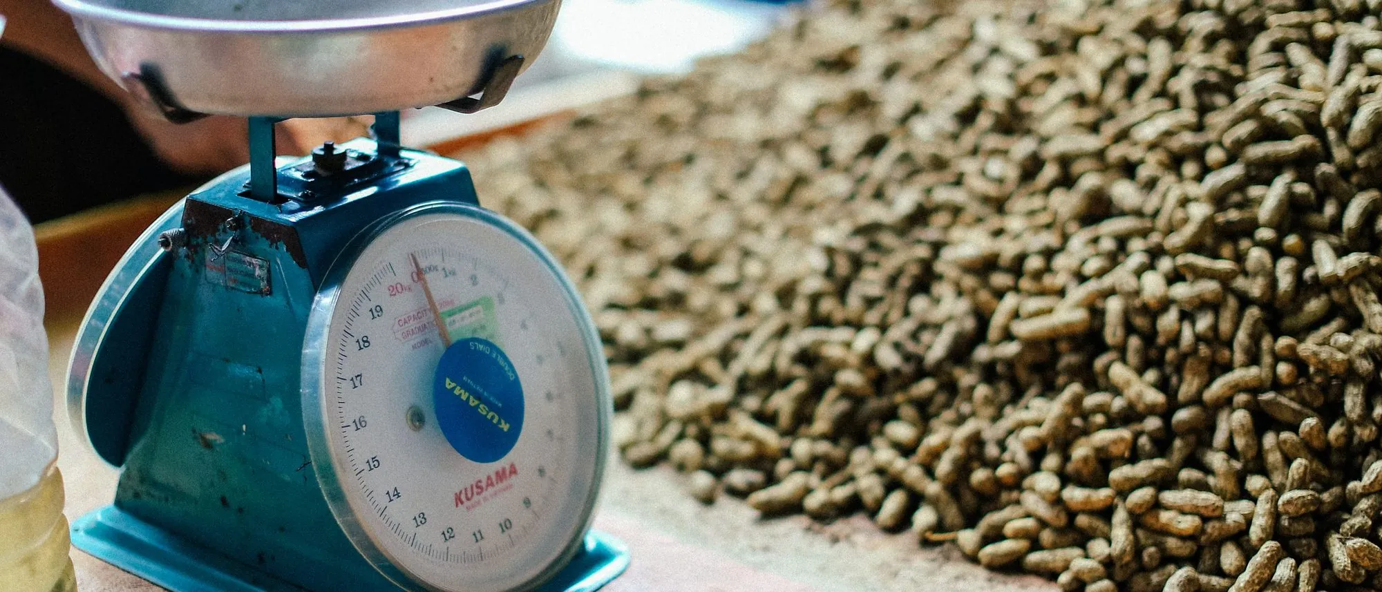 A vintage weighing scale beside a pile of peanuts in natural light.