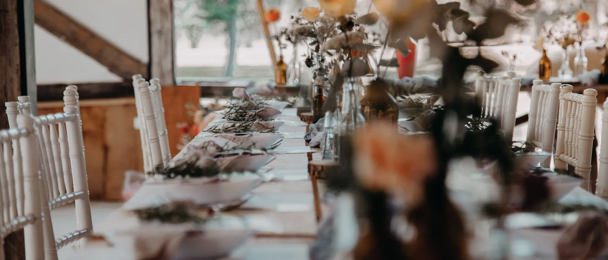 A long table laid with plates, glasses and flowers before guests arrive.