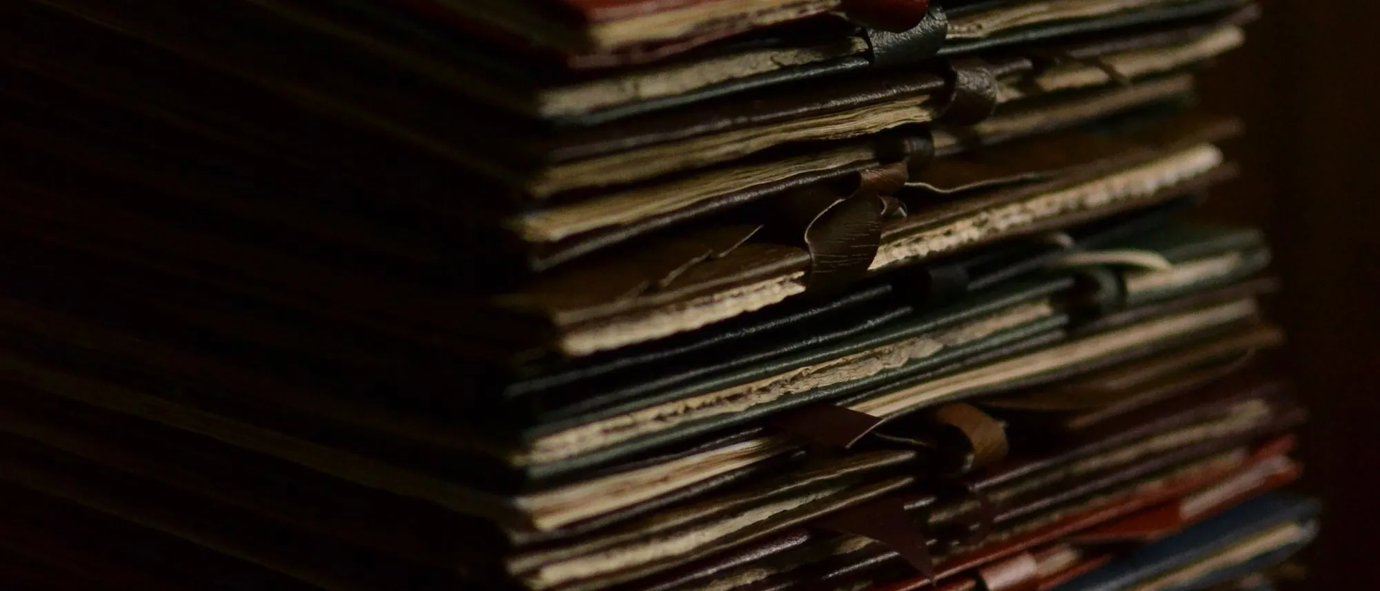 A tall stack of worn file folders tied with ribbon on a dark wooden desk