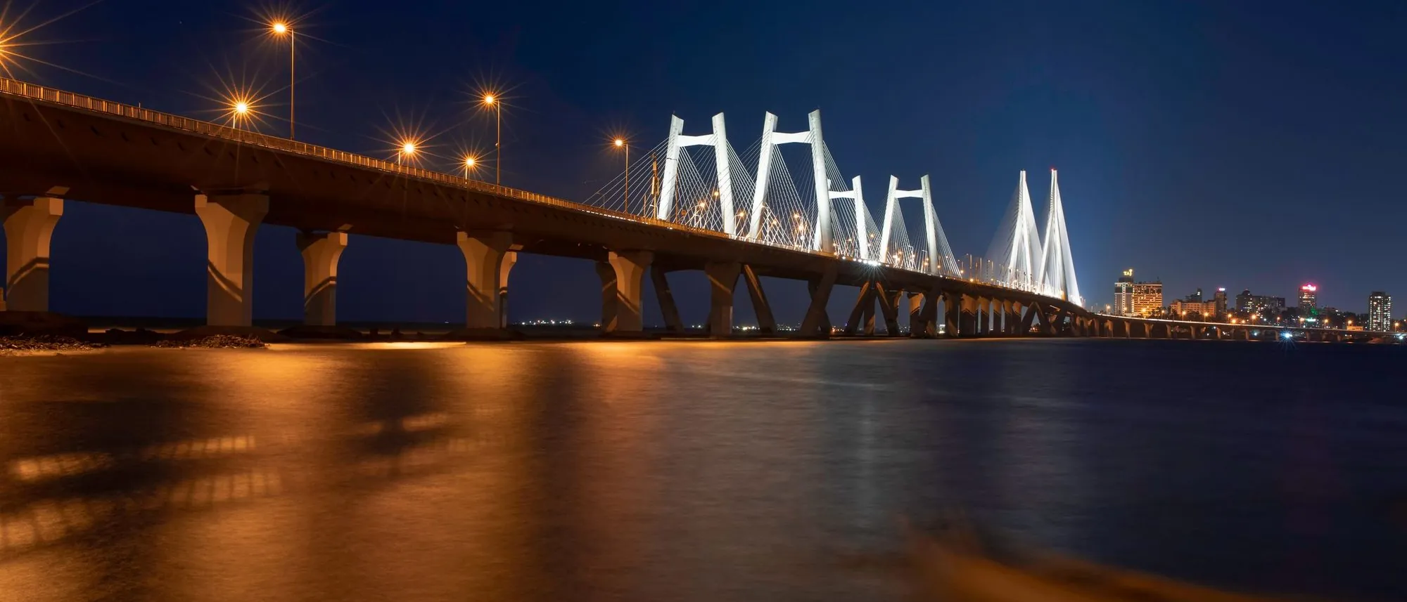 The Bandra-Worli Sea Link in Mumbai lit up at night over dark water.