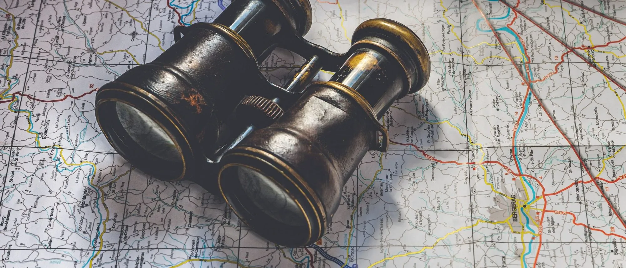 A pair of antique binoculars lying on a detailed road map