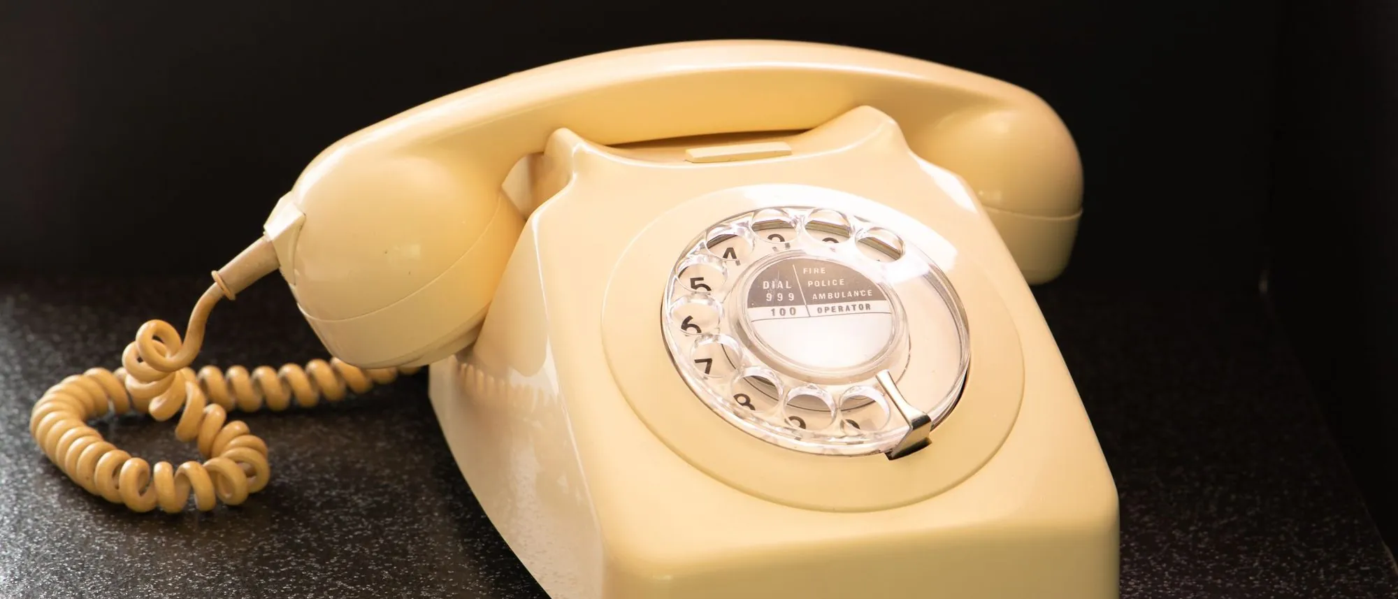 A cream rotary telephone on a dark surface