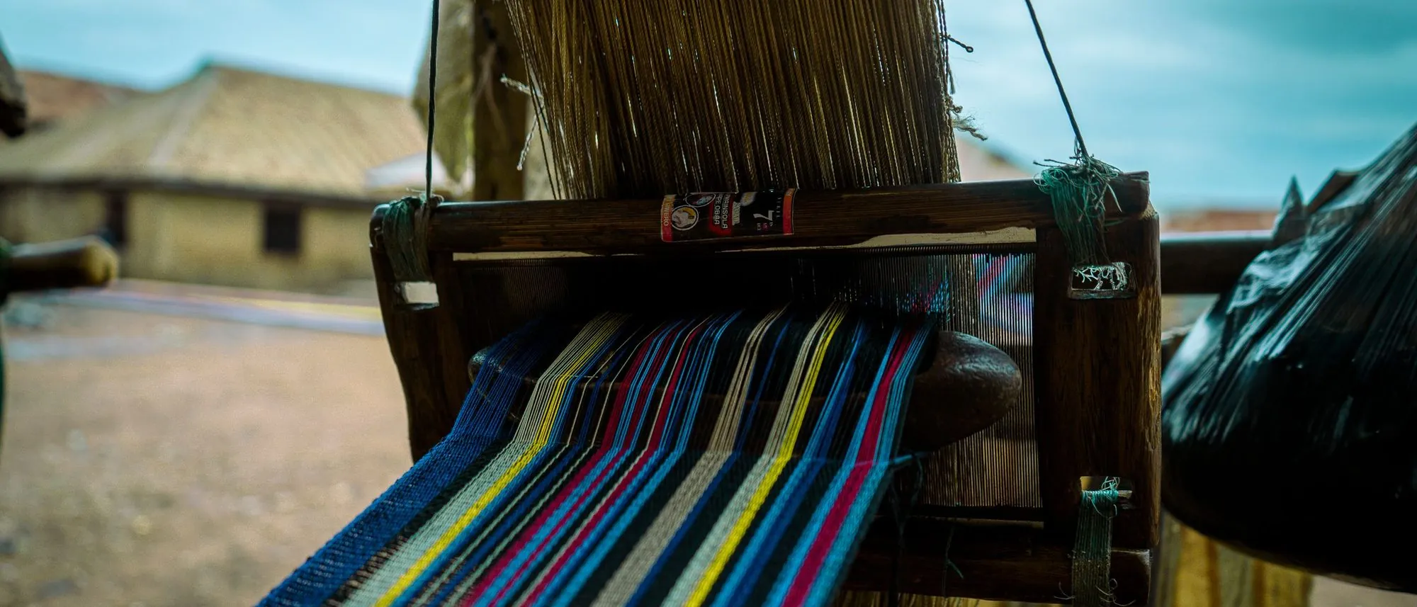 A handloom mid-weave with coloured threads stretched across the frame.