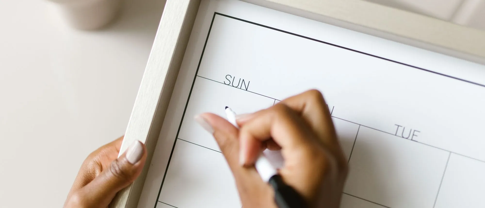 Hands hold a wall calendar and write on it with a marker.
