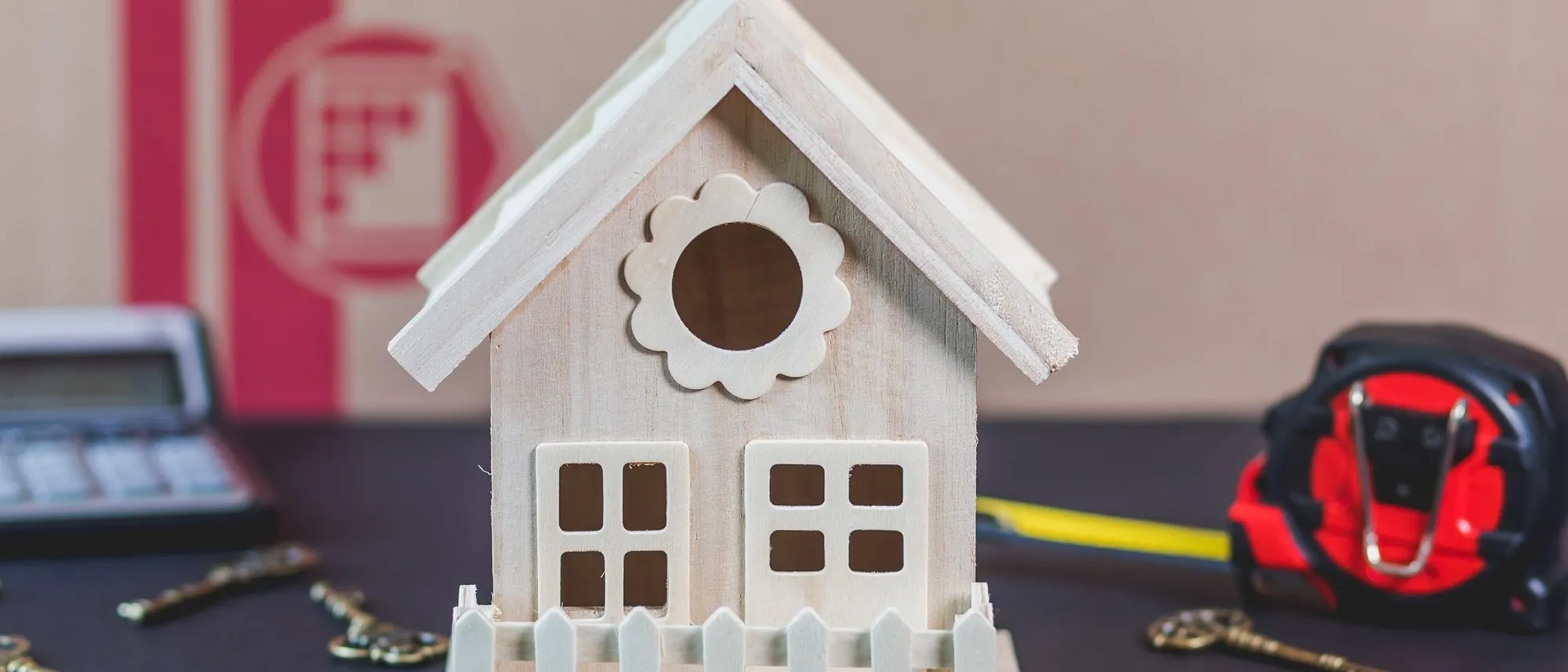 A small white wooden model house ringed by old iron keys on a black surface.