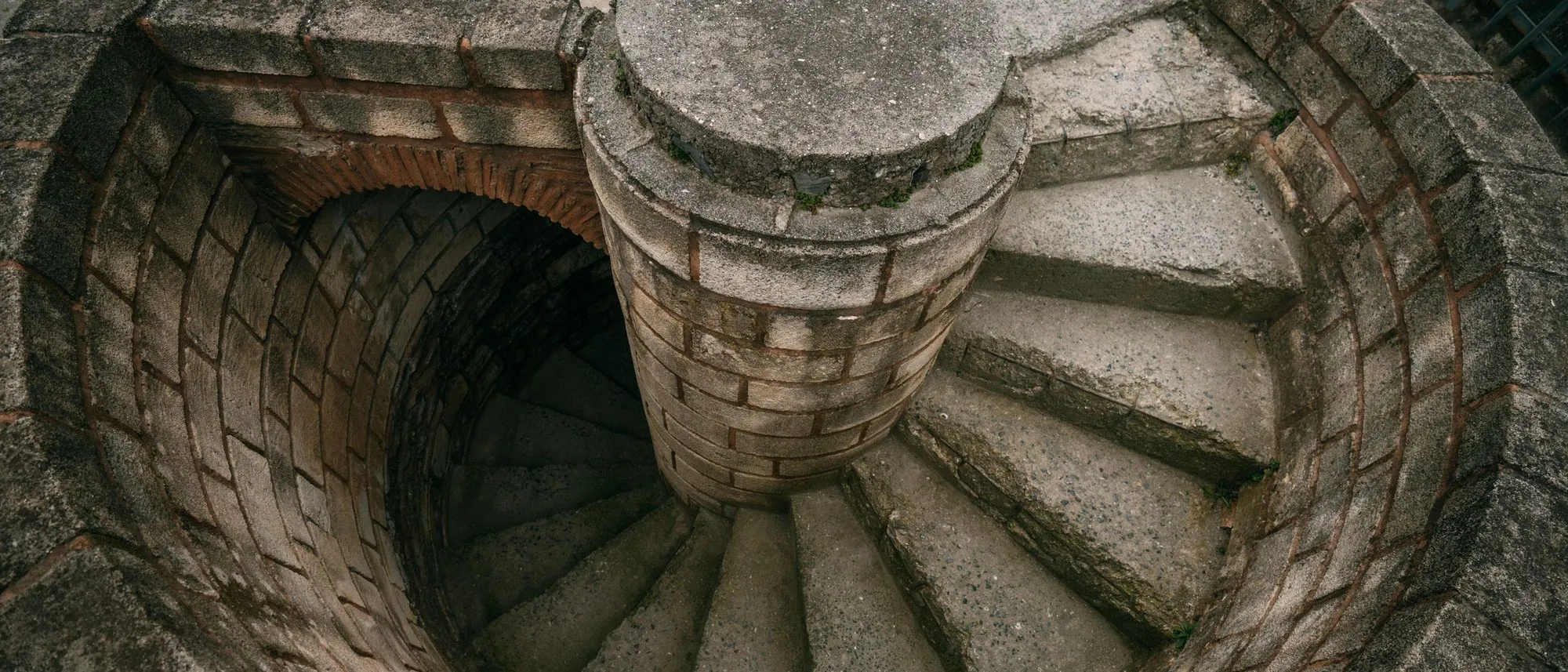 A stone staircase spiralling down around a central column, seen from above.