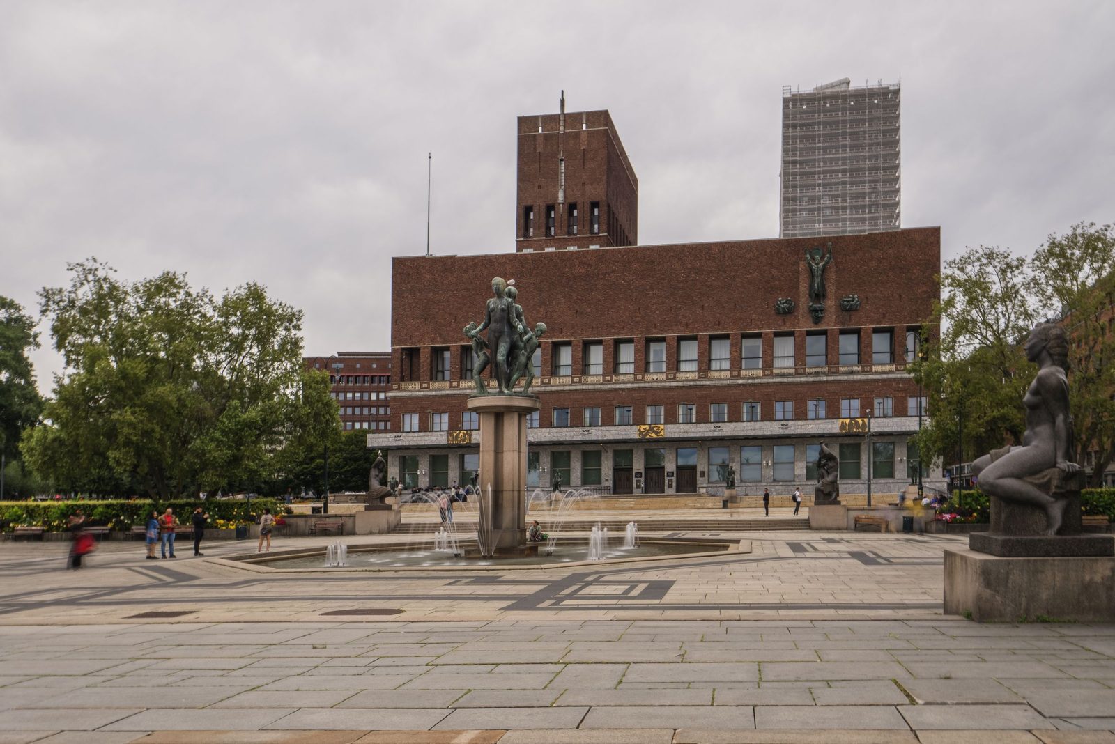 Oslo City Hall, a red-brick building with two towers, behind a paved square with a fountain and bronze statues