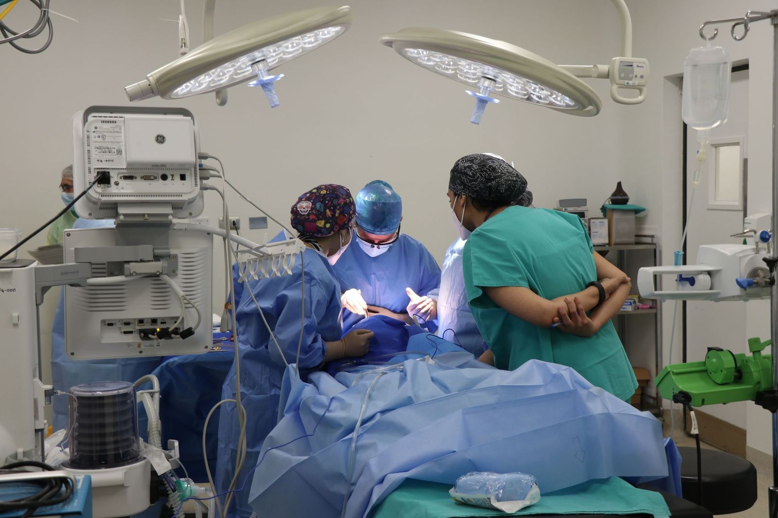 A surgical team in gowns and caps seen from behind under theatre lights