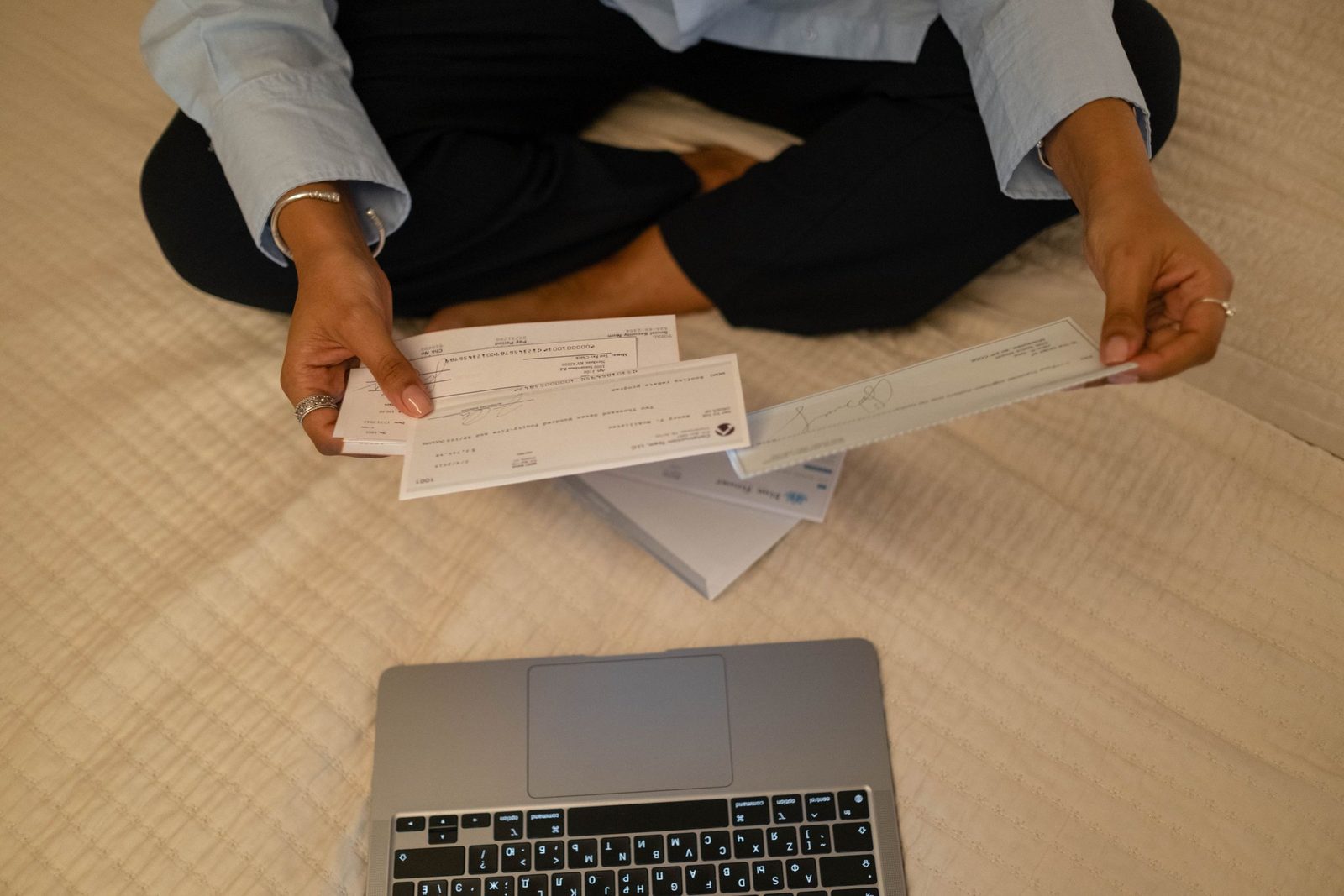 Hands hold a set of cheques beside an open laptop.