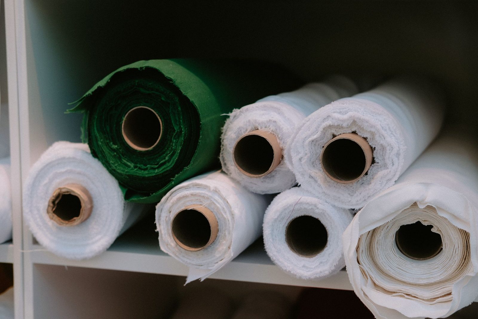 Rolls of fabric in many colours stacked on a storage shelf.