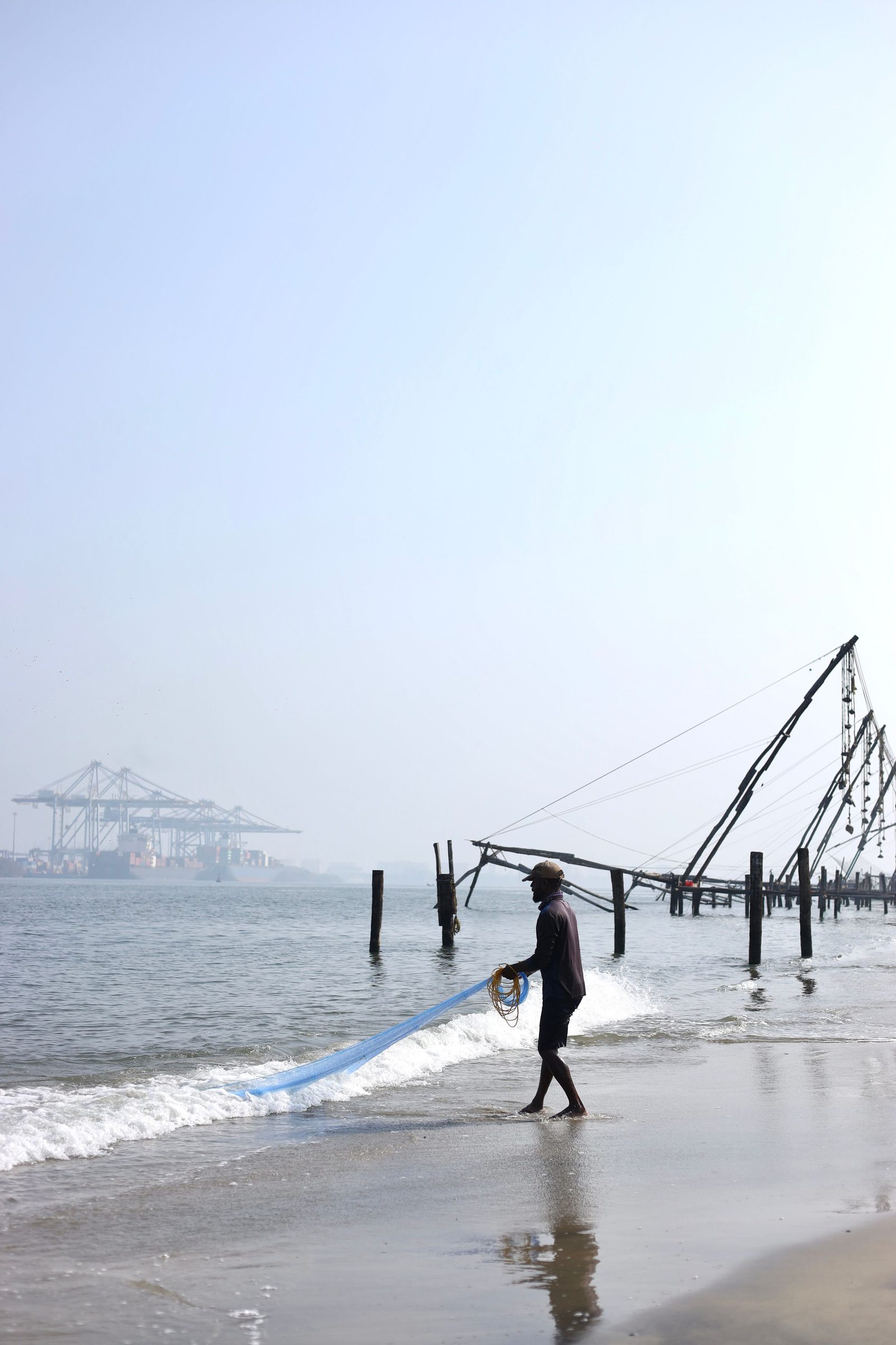 A fisherman casts a hand net from the beach at Kochi with the large lift nets behind him.