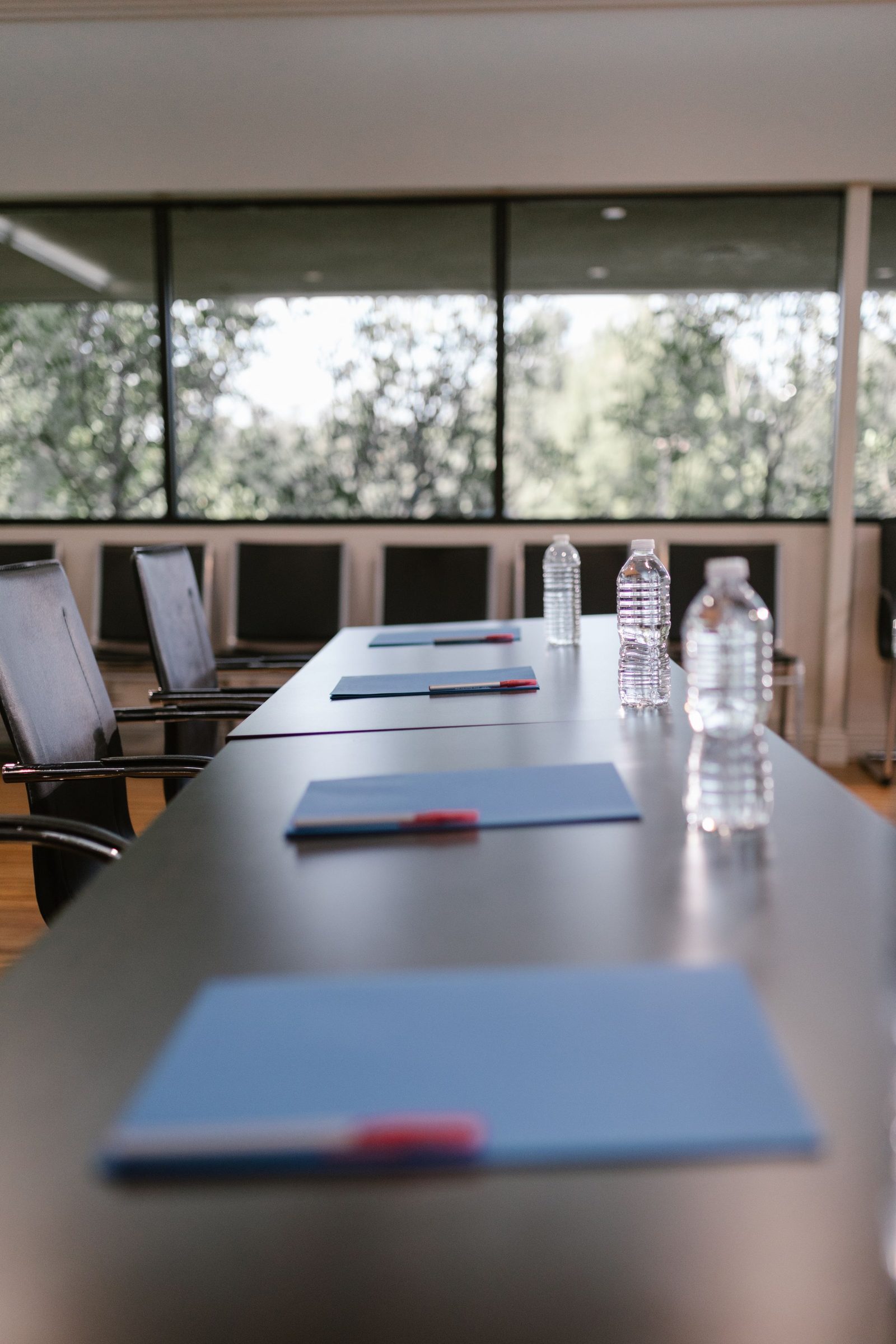 A conference table set with water bottles and notebooks beside a window.