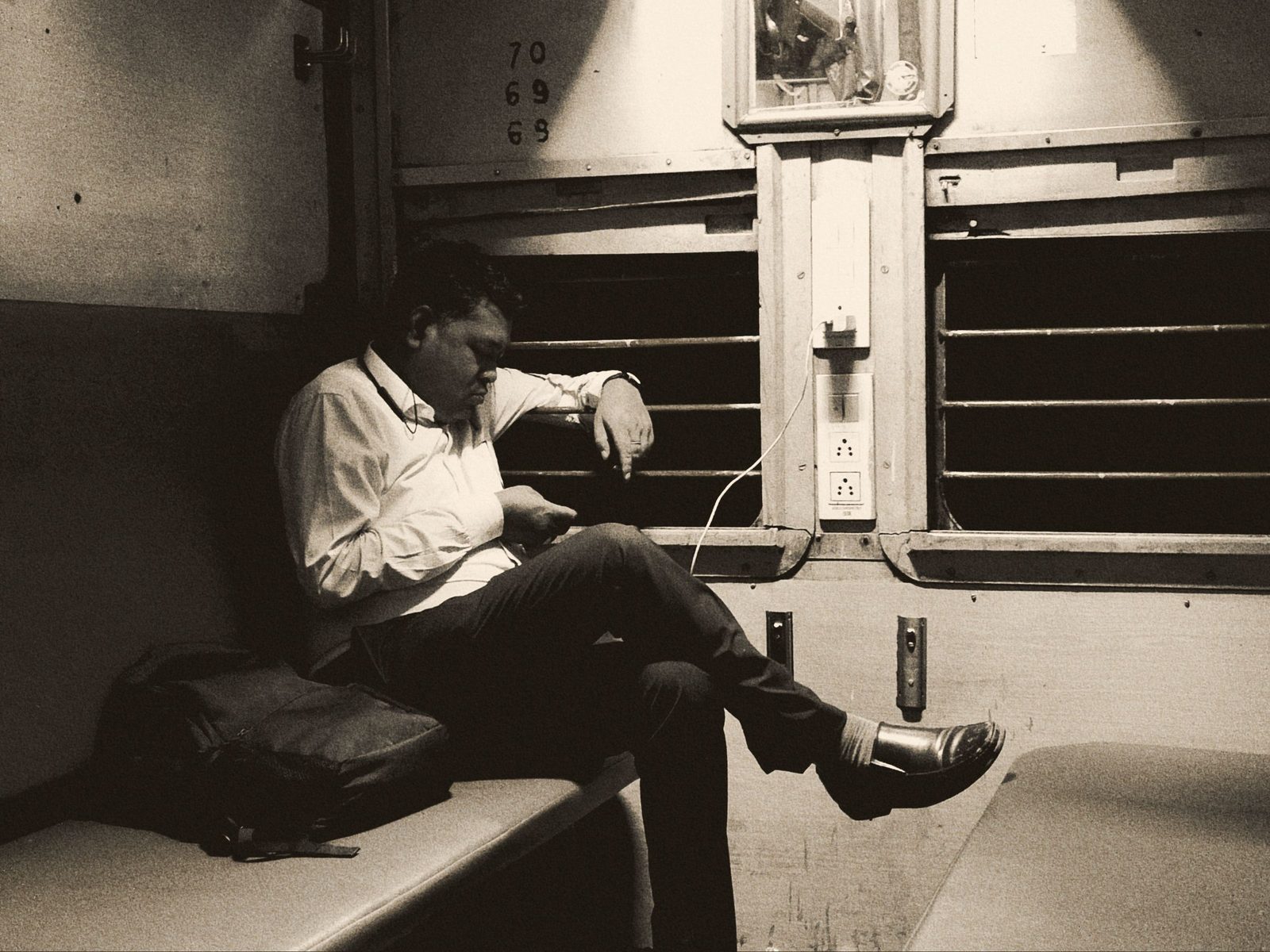 A man sits alone in a train carriage at night looking at his phone.