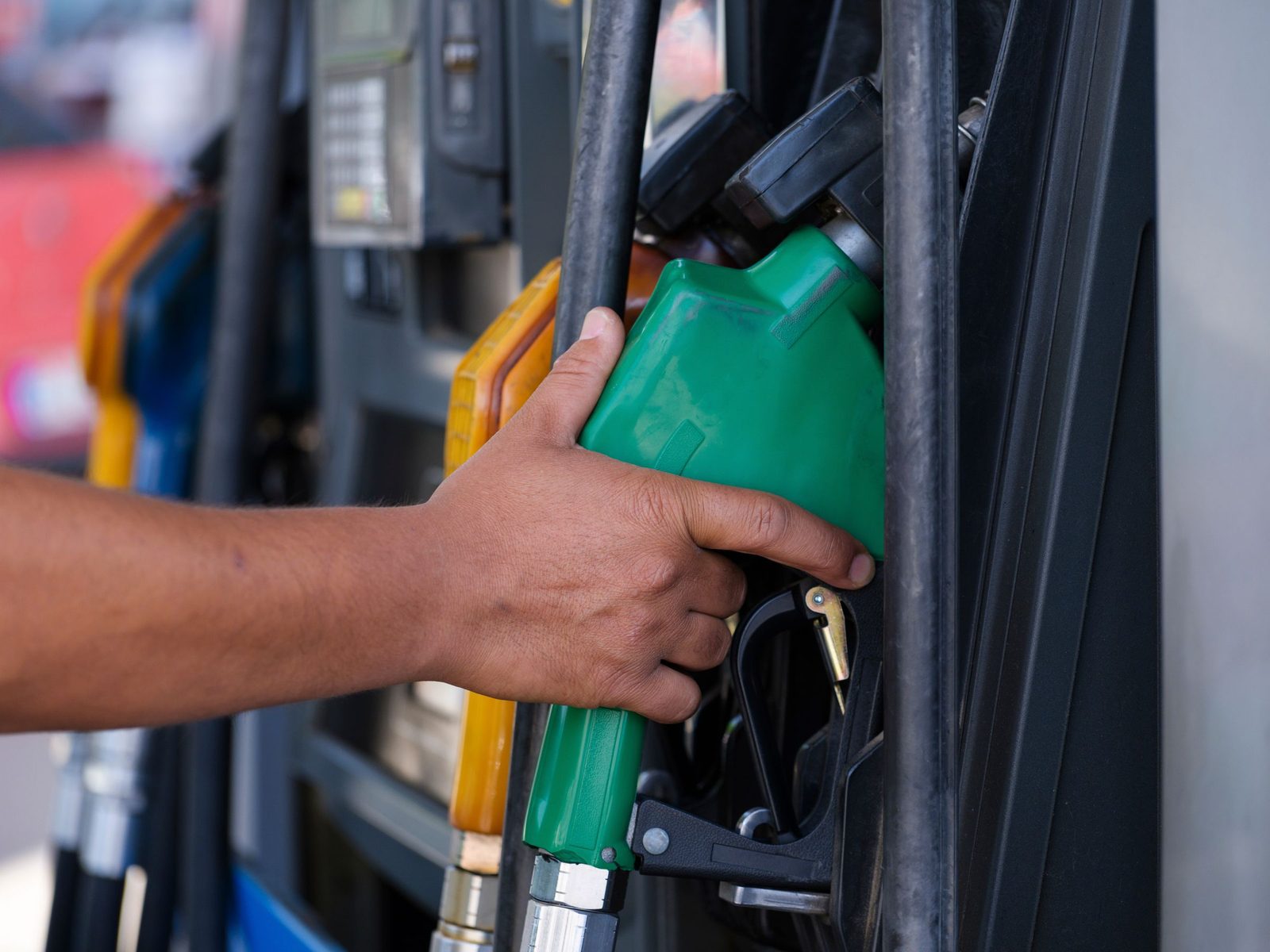 A hand holds a green fuel nozzle at a petrol pump.