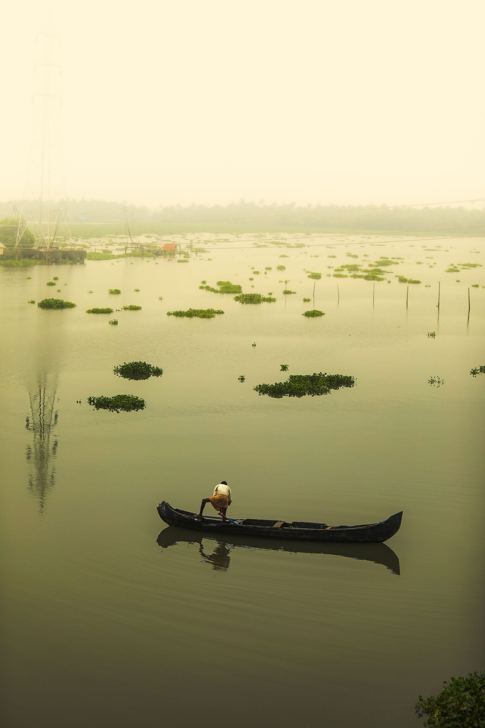 A single canoe on calm backwaters under a misty morning sky with greenery on the banks.