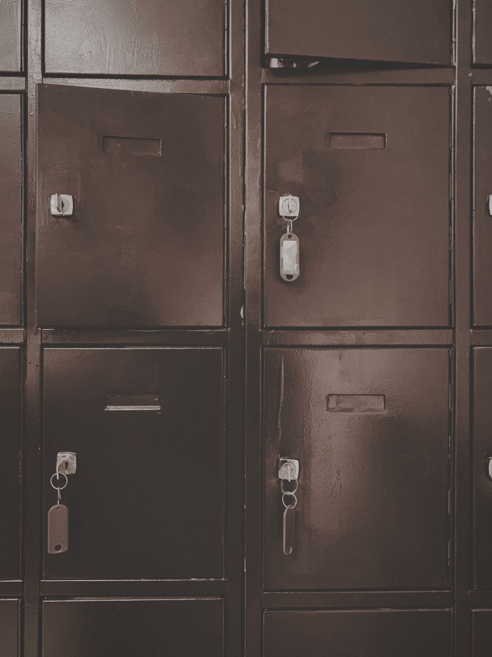 A wall of old metal lockers closed with padlocks in sepia tones.