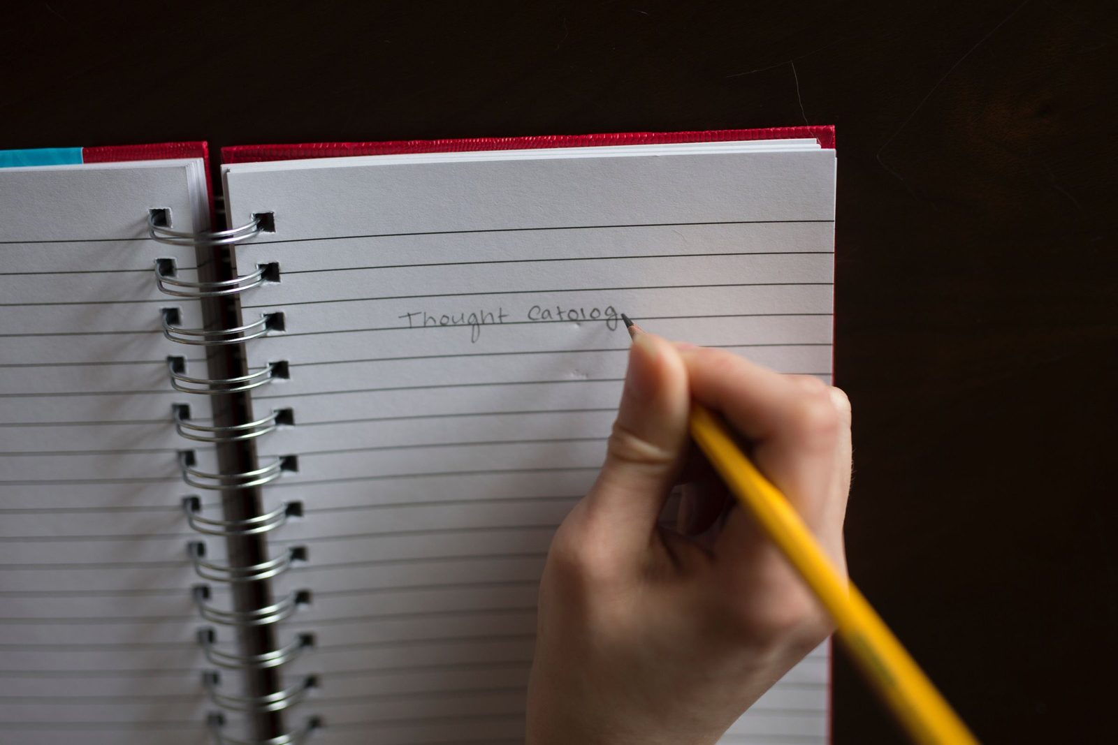 A hand writing with a pencil in a spiral-bound notebook with lined pages.