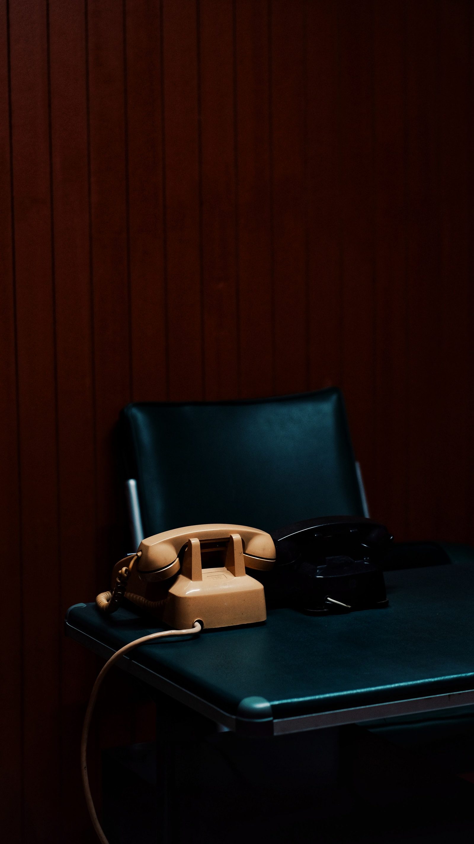 Two classic telephones on a desk in a dim office panelled in dark wood.