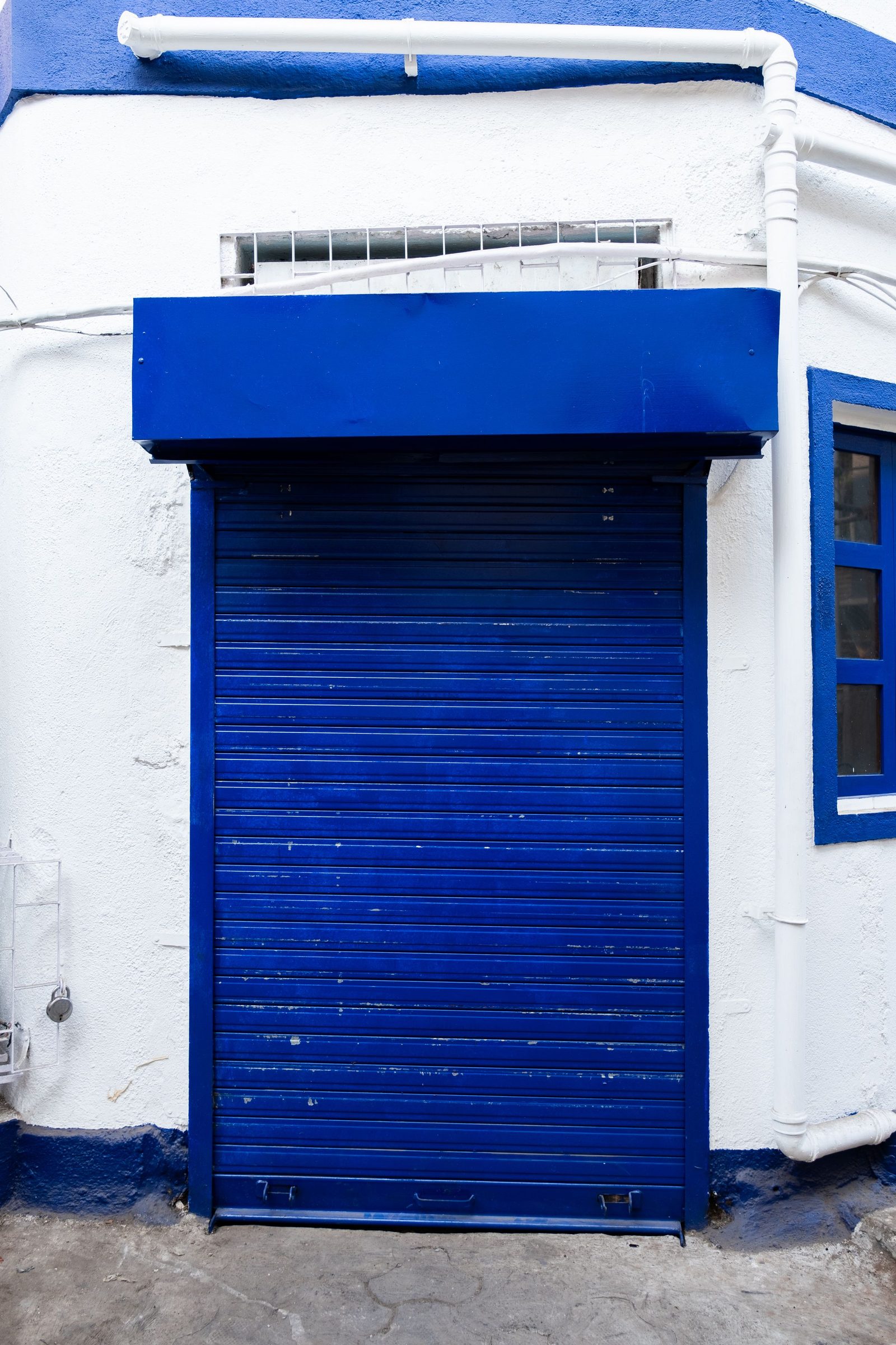 A closed blue roll-up shutter set into a white building front in Mumbai.