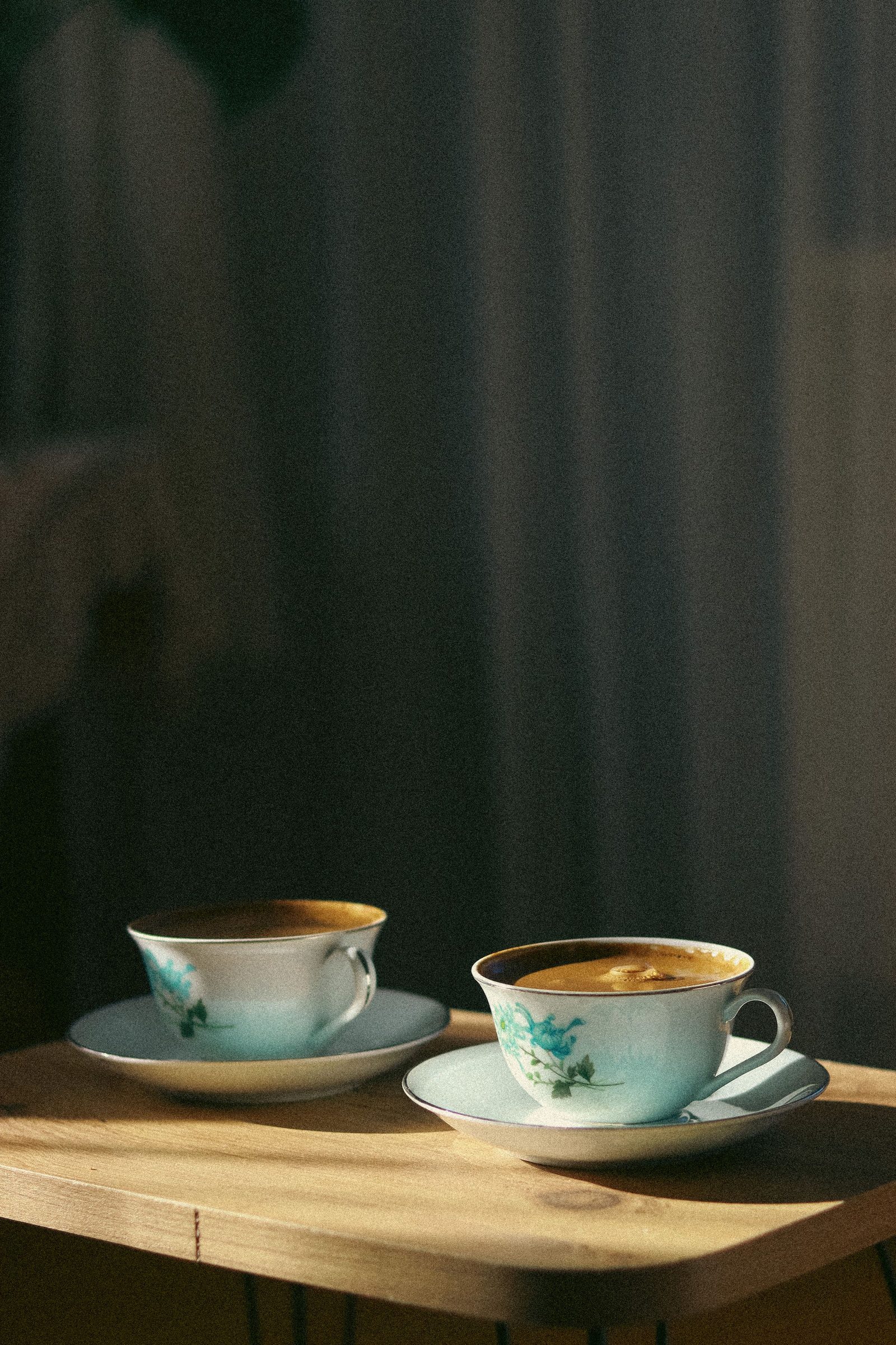 Two porcelain coffee cups rest on a wooden table indoors.