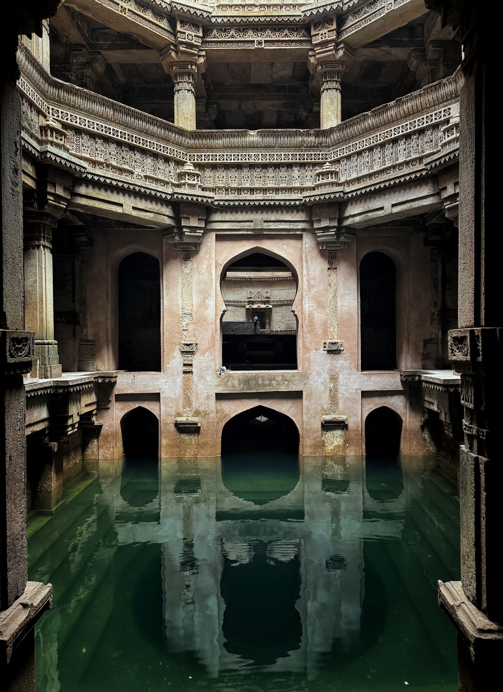 Carved stone galleries of a stepwell in Gujarat reflected in still water.
