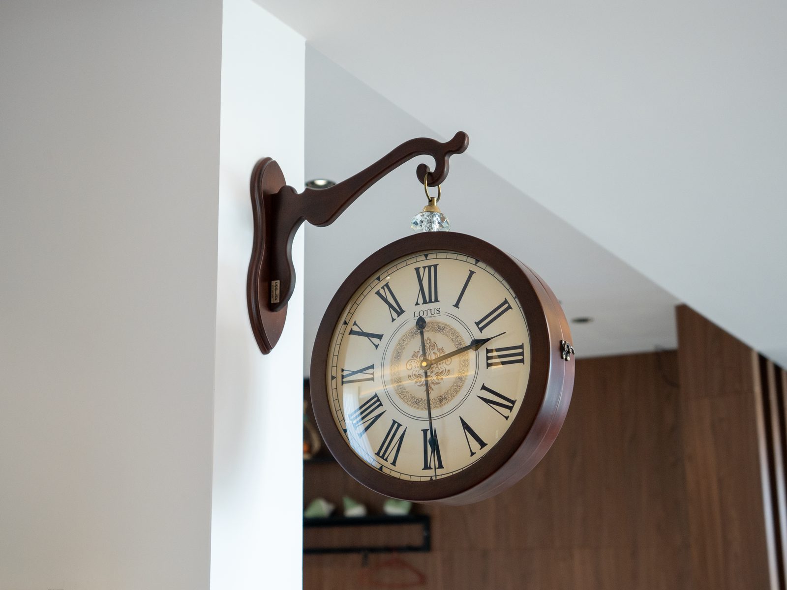 A vintage wall clock with Roman numerals hangs on a plain wall.