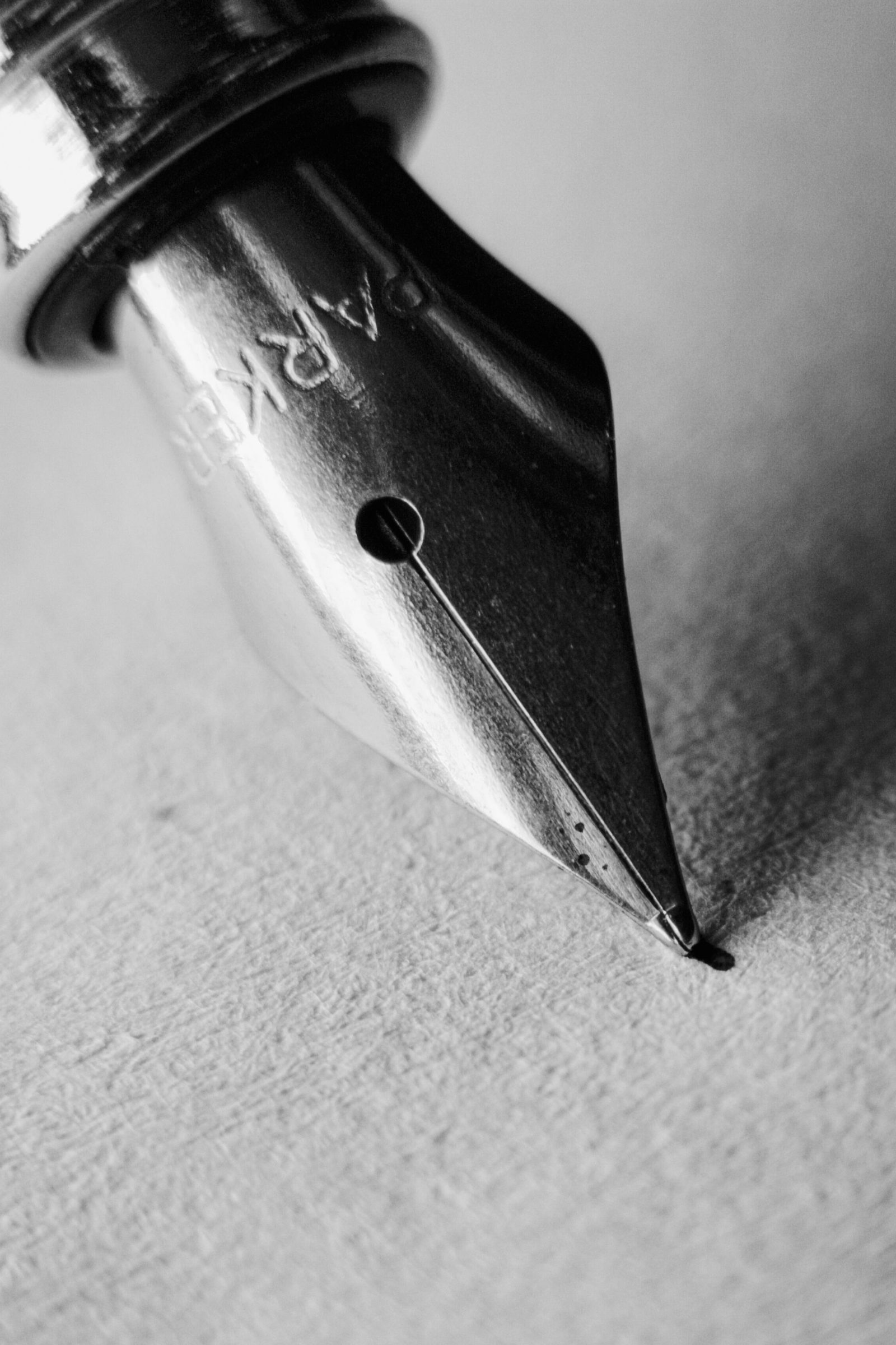 A fountain pen nib rests on grainy paper in black and white.