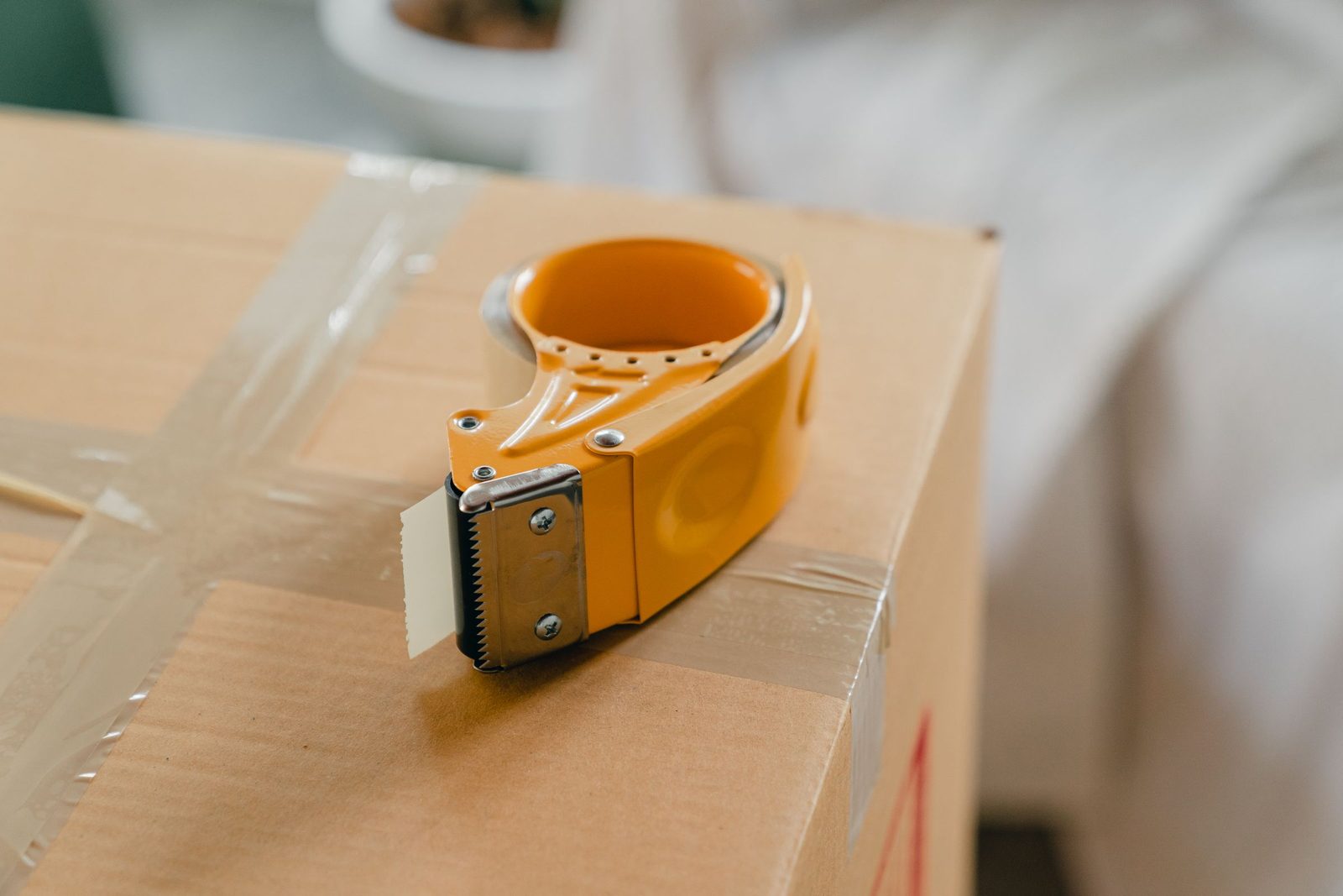 A yellow tape dispenser resting on a sealed cardboard box.