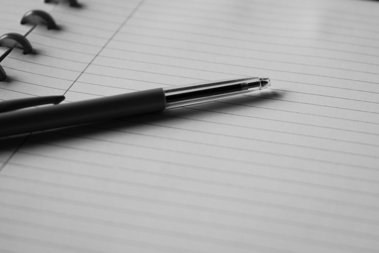 A pen rests on the open lined page of a notebook in black and white.