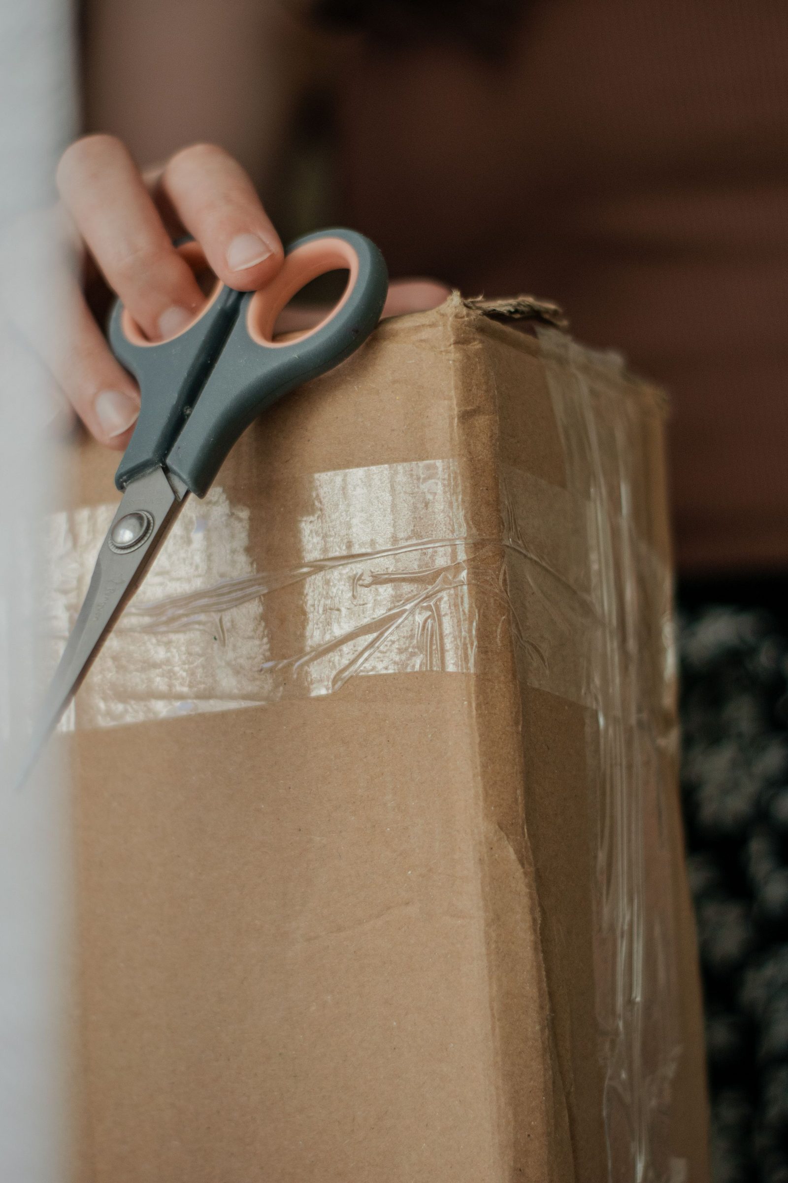 A person opens a taped cardboard box with a pair of scissors.