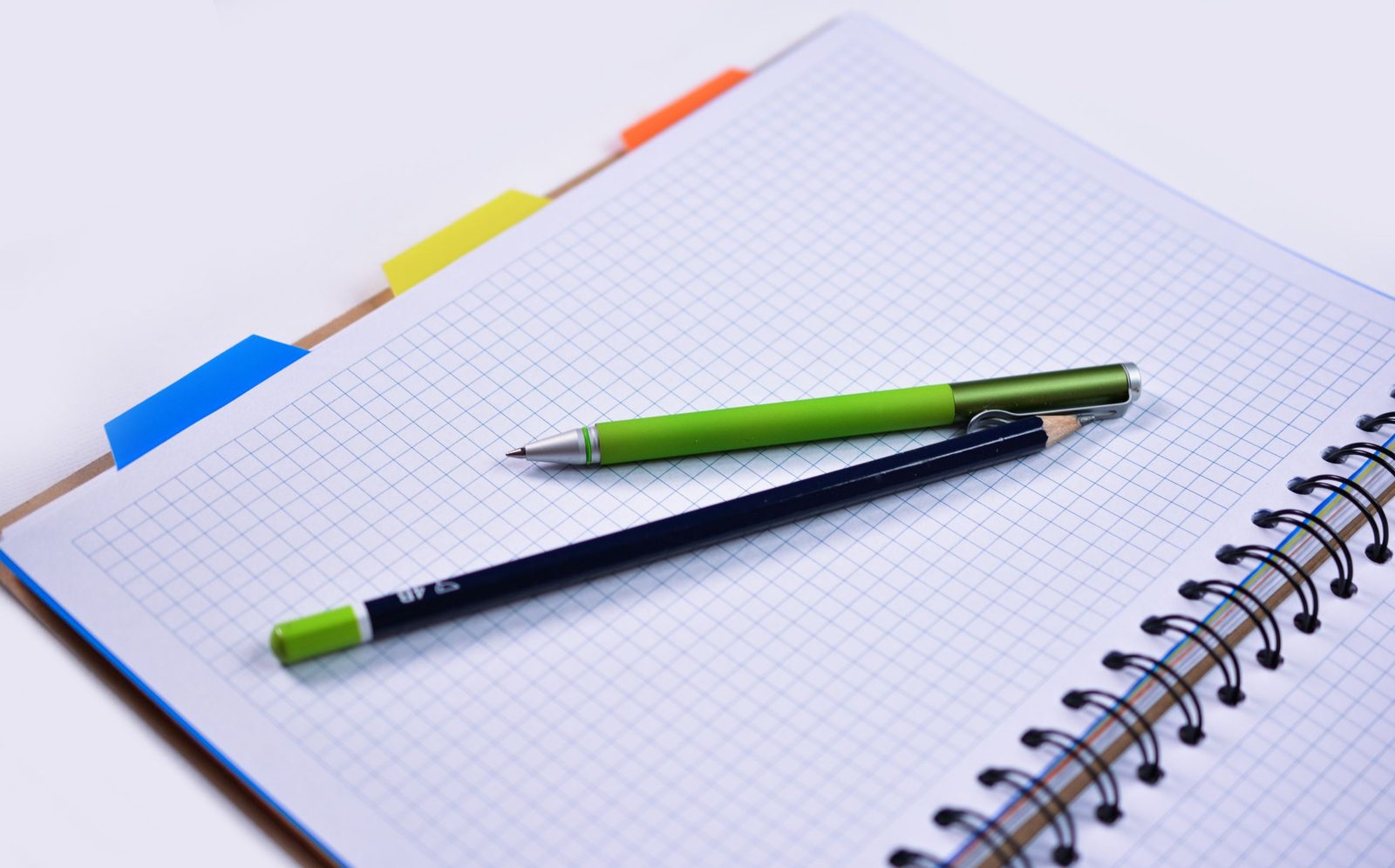 An open spiral notebook of graph paper with a pen and a pencil.