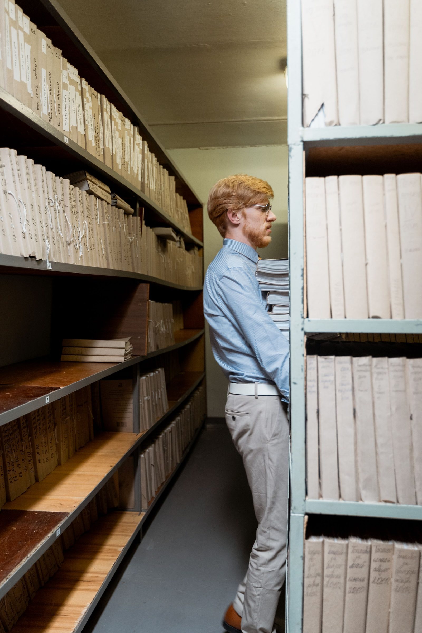 A man places a stack of documents on a shelf in a dimly lit archive room.